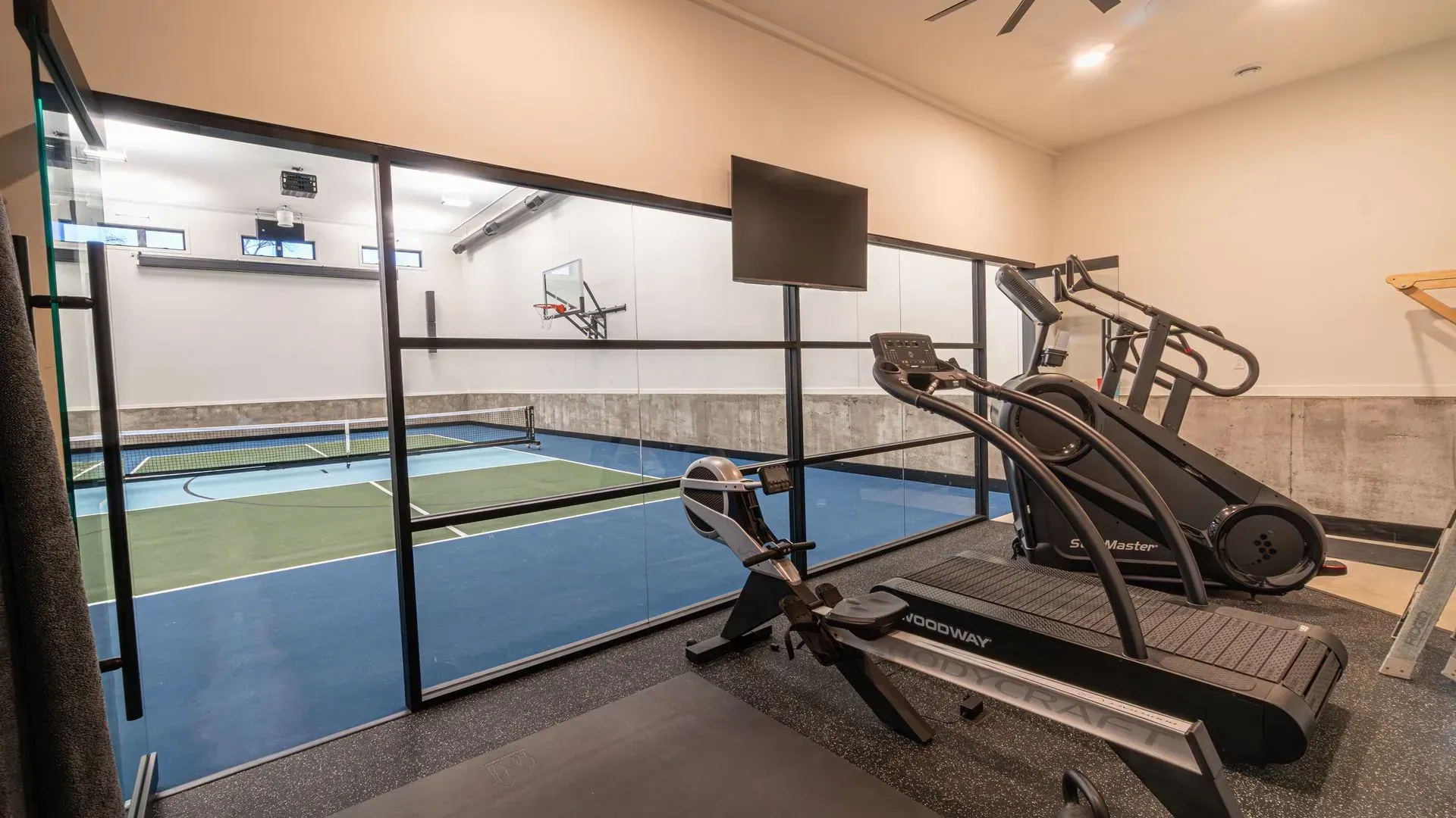 Gym interior with exercise equipment near a glass-walled sports court.
