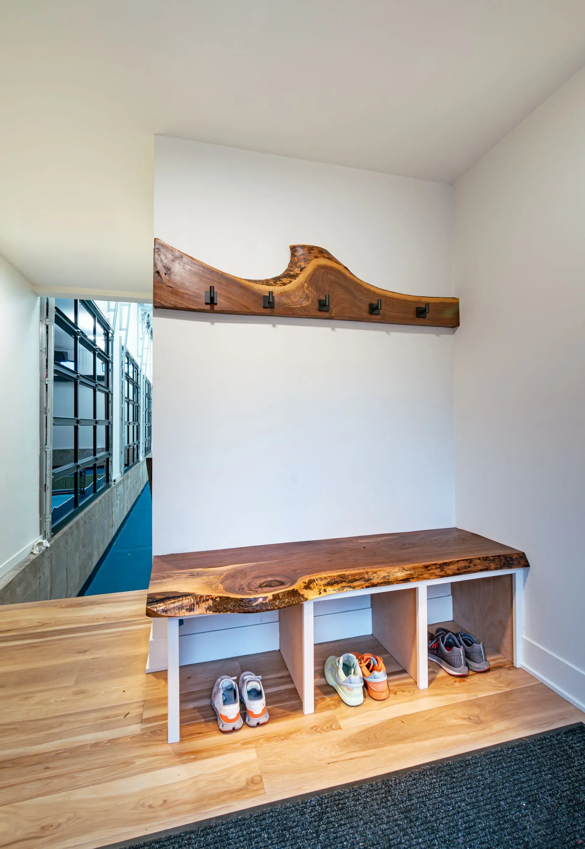 Wooden entryway bench with shoe storage and coat rack against a white wall.