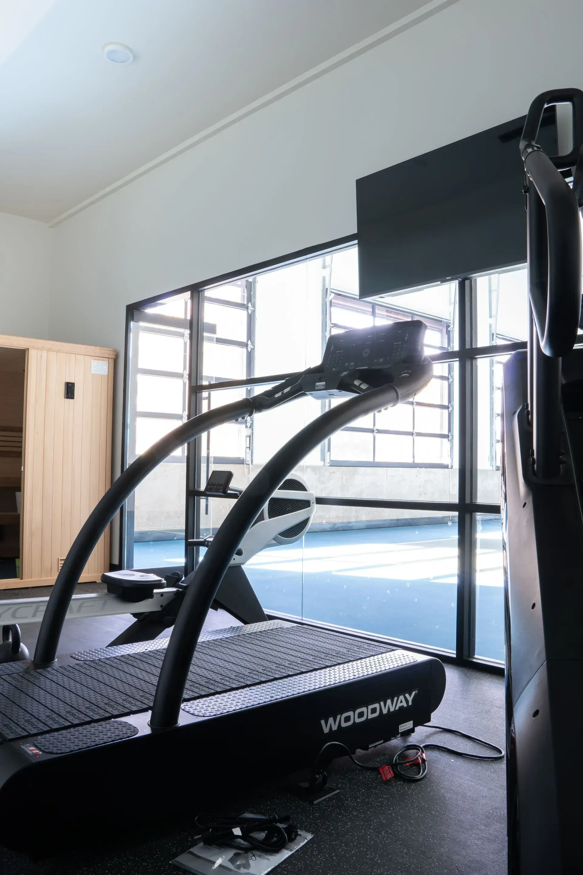 Gym interior with treadmill and stair climber, windows, and sauna.