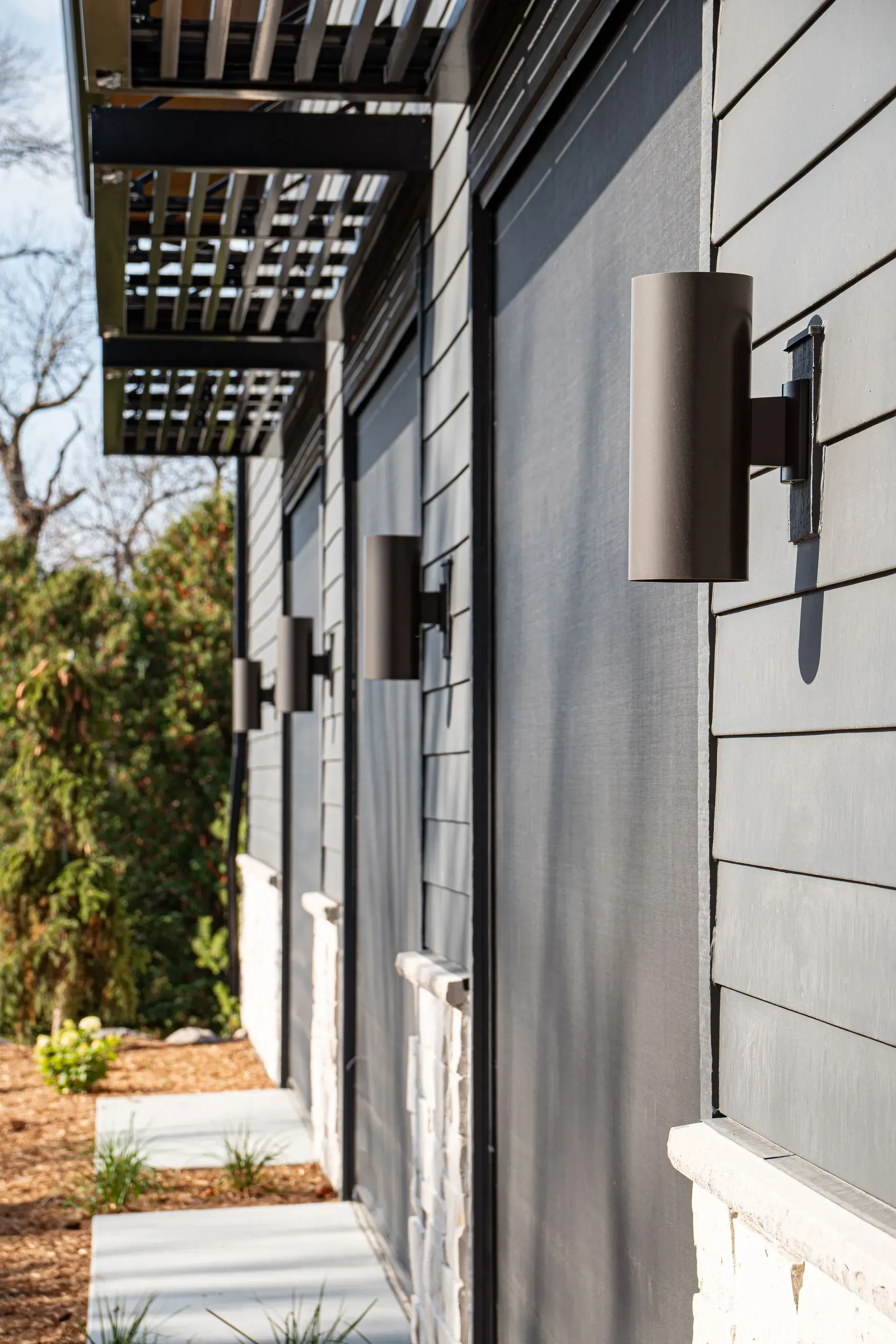Gray building exterior with cylindrical wall lights and a slatted awning.