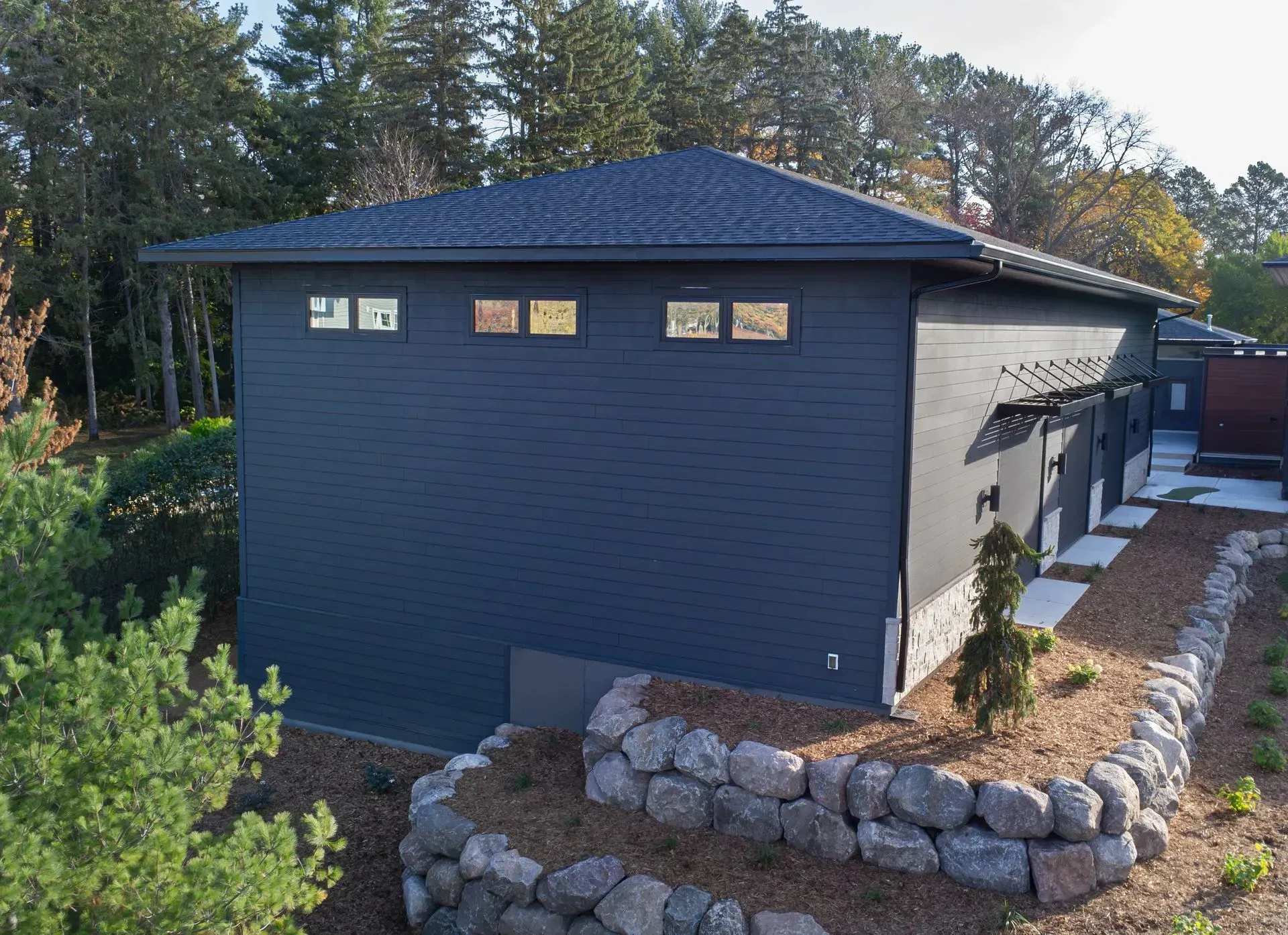 Dark blue modern house with a black roof and stone retaining wall.