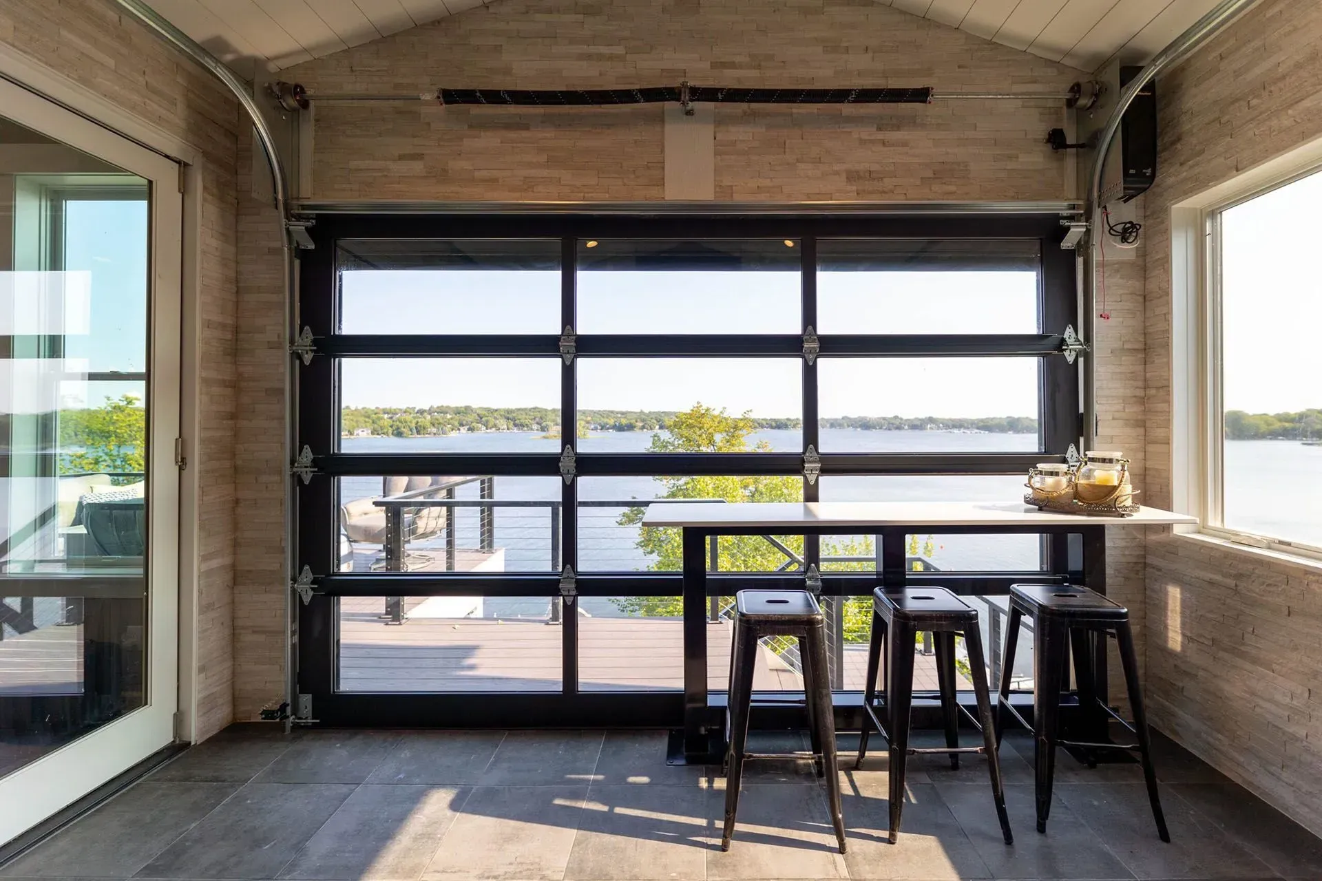Sunroom with garage door overlooking water, table, bar stools, and window.