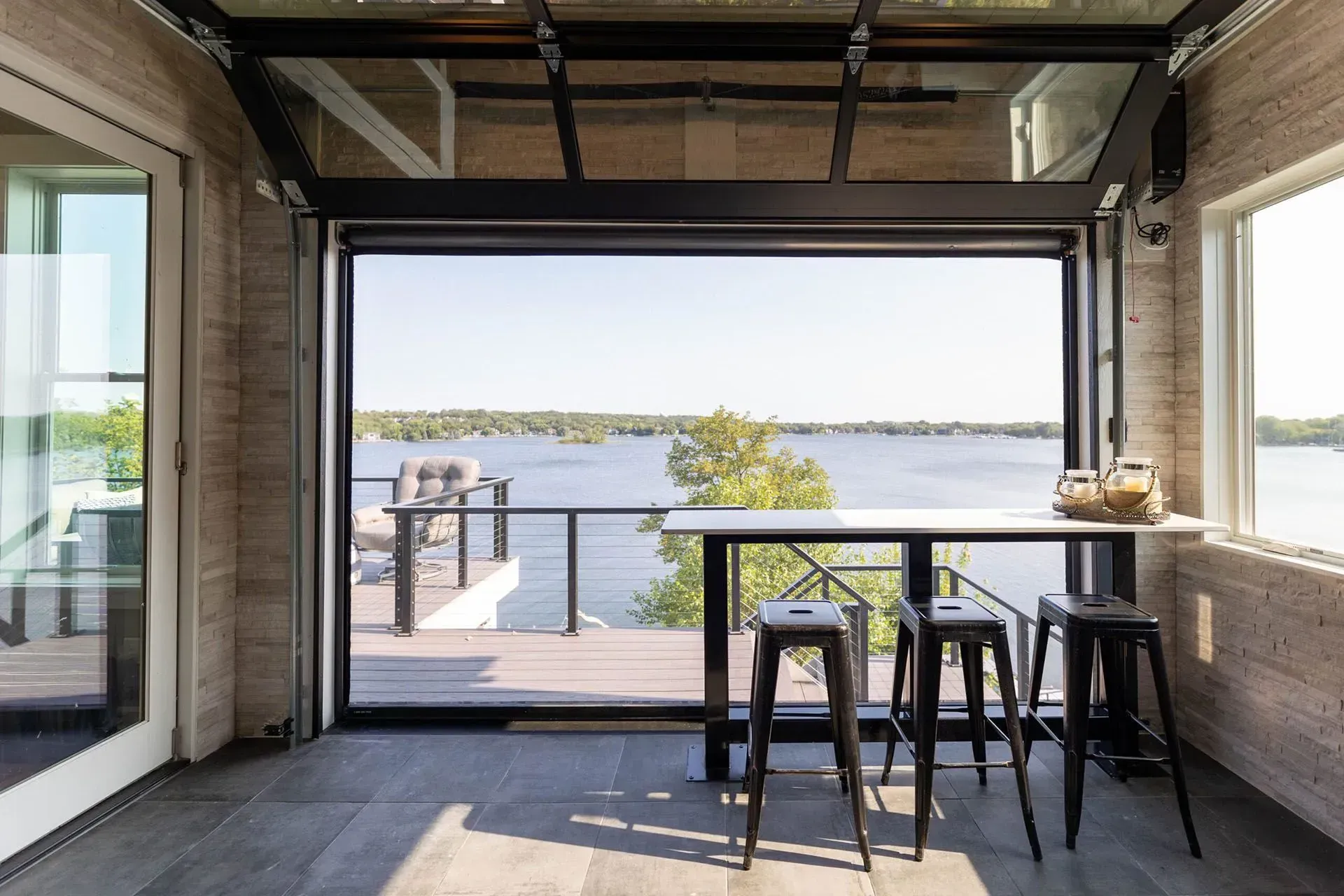 Interior room with glass folding door open to lake view. Table with stools, modern design.