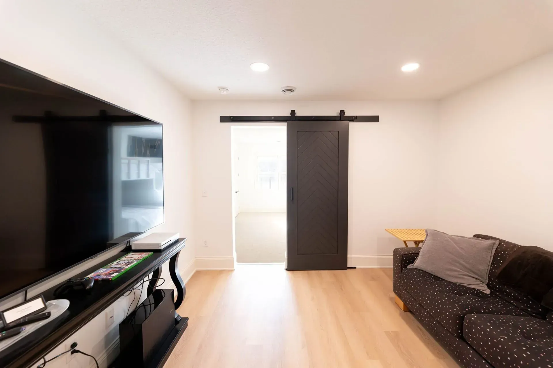 Living room with a large TV, black barn door, and patterned sofa.