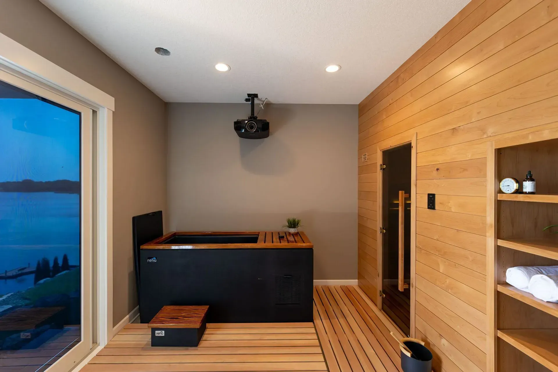 Interior with black soaking tub, wooden sauna, and shelving. Light wood floors and walls, sliding glass door.