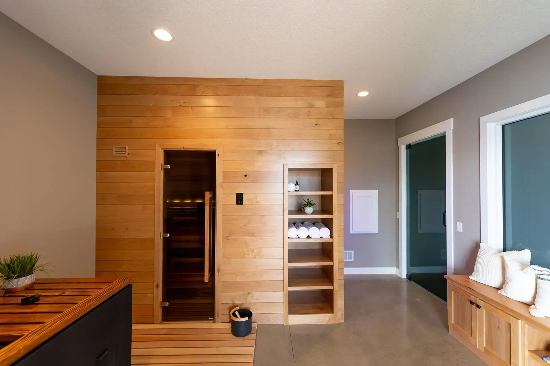 Sauna room with wooden paneling, glass door, shelves, and gray walls.