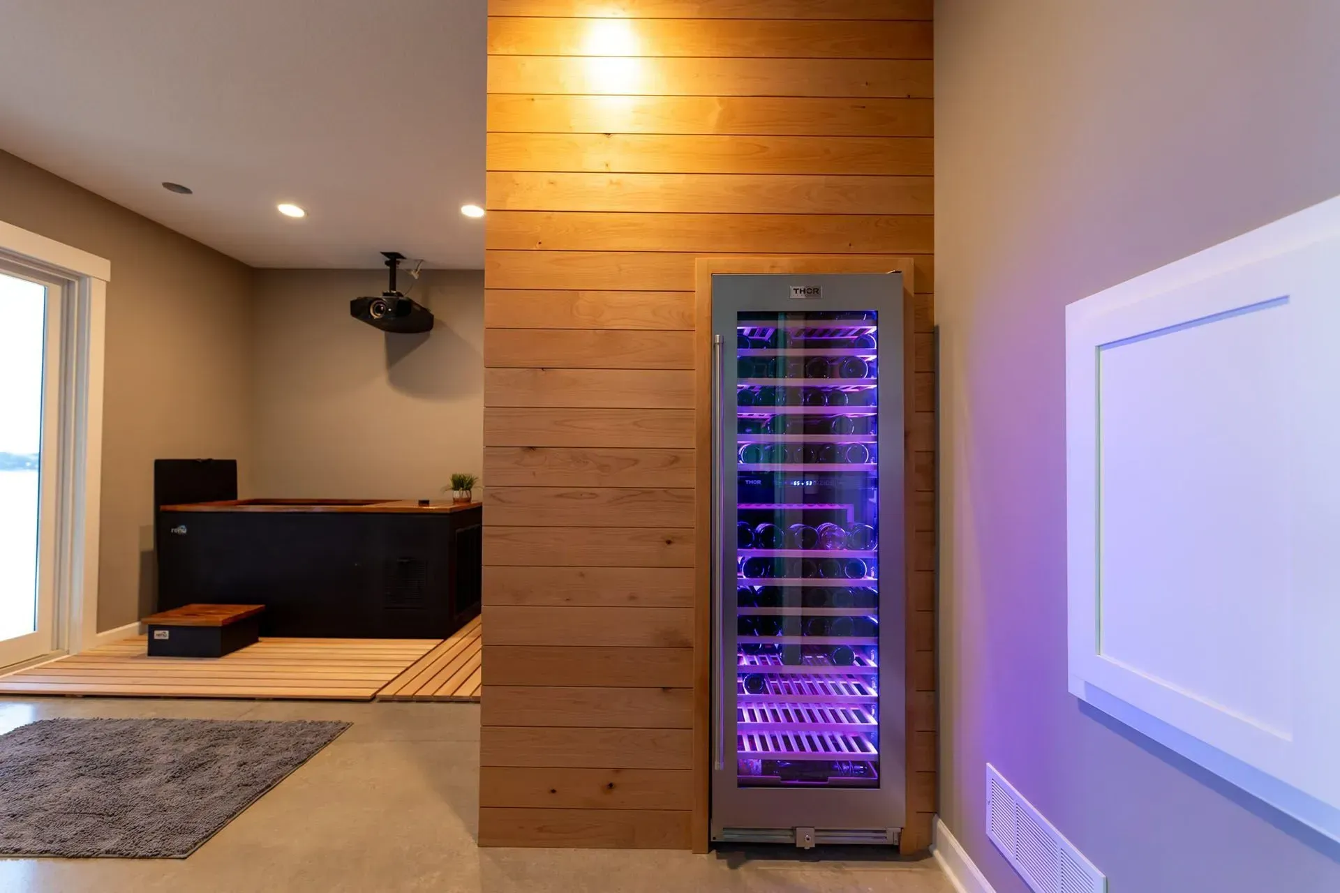 Wine cooler with purple lighting in a room with wood paneling and a home theater setup.