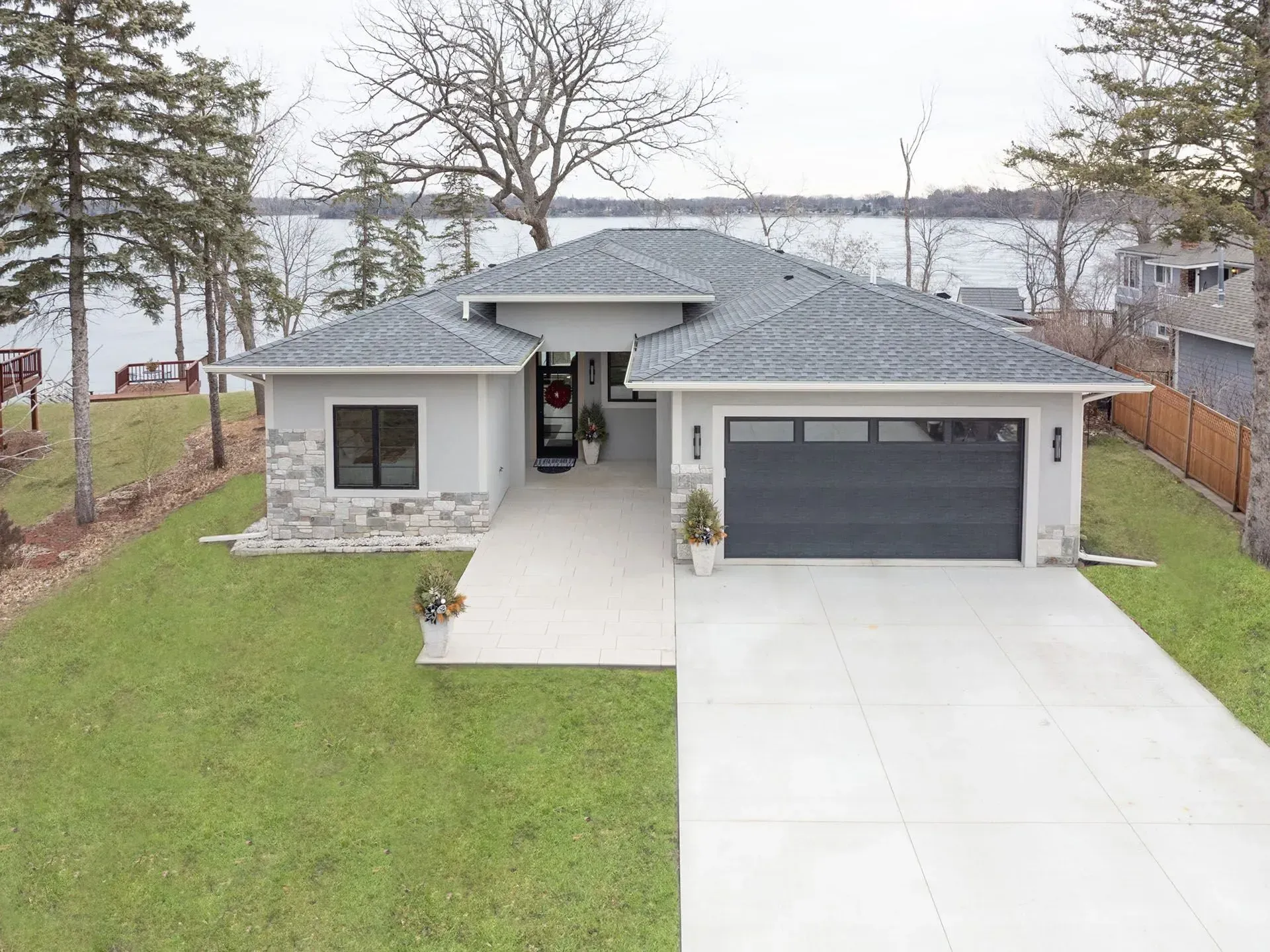 Modern gray house with black garage door, stone accents, and lake view.