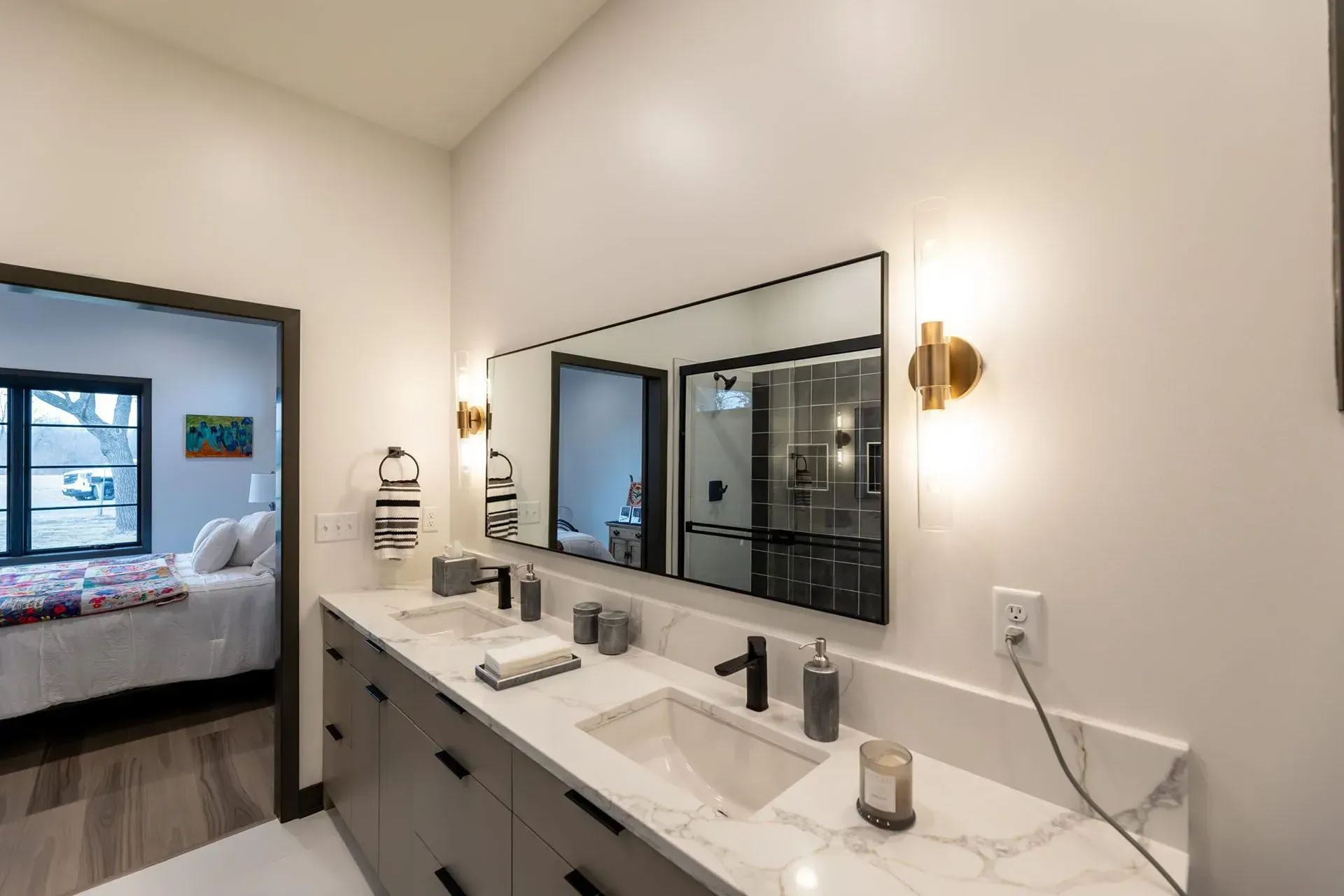 Modern bathroom with gray cabinets, marble countertop, and double sinks, with a bedroom doorway in the background.