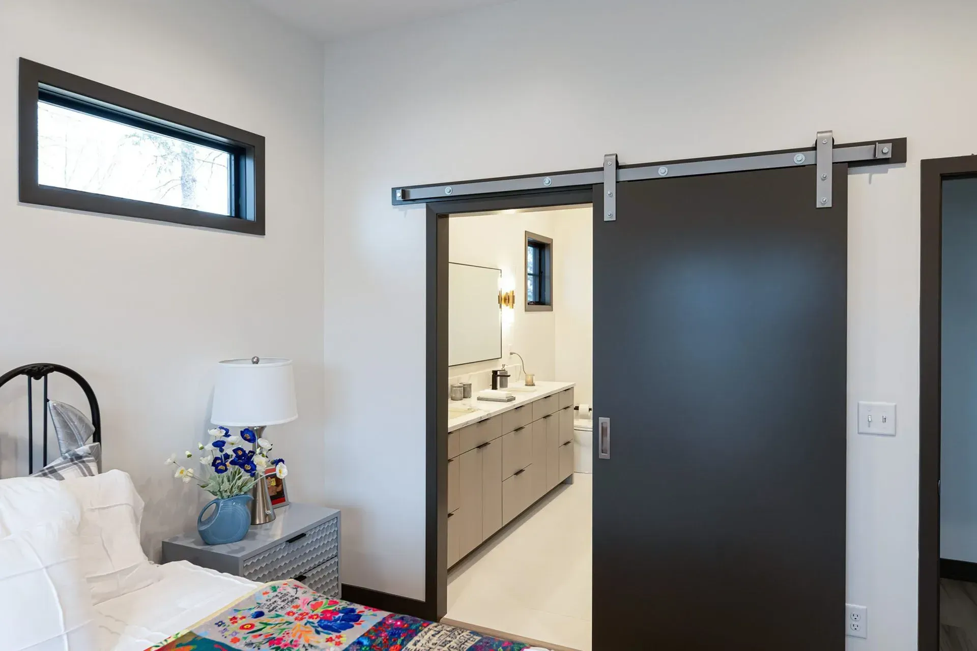 Bedroom with a dark gray sliding door open to a bathroom with gray cabinets and a mirror.