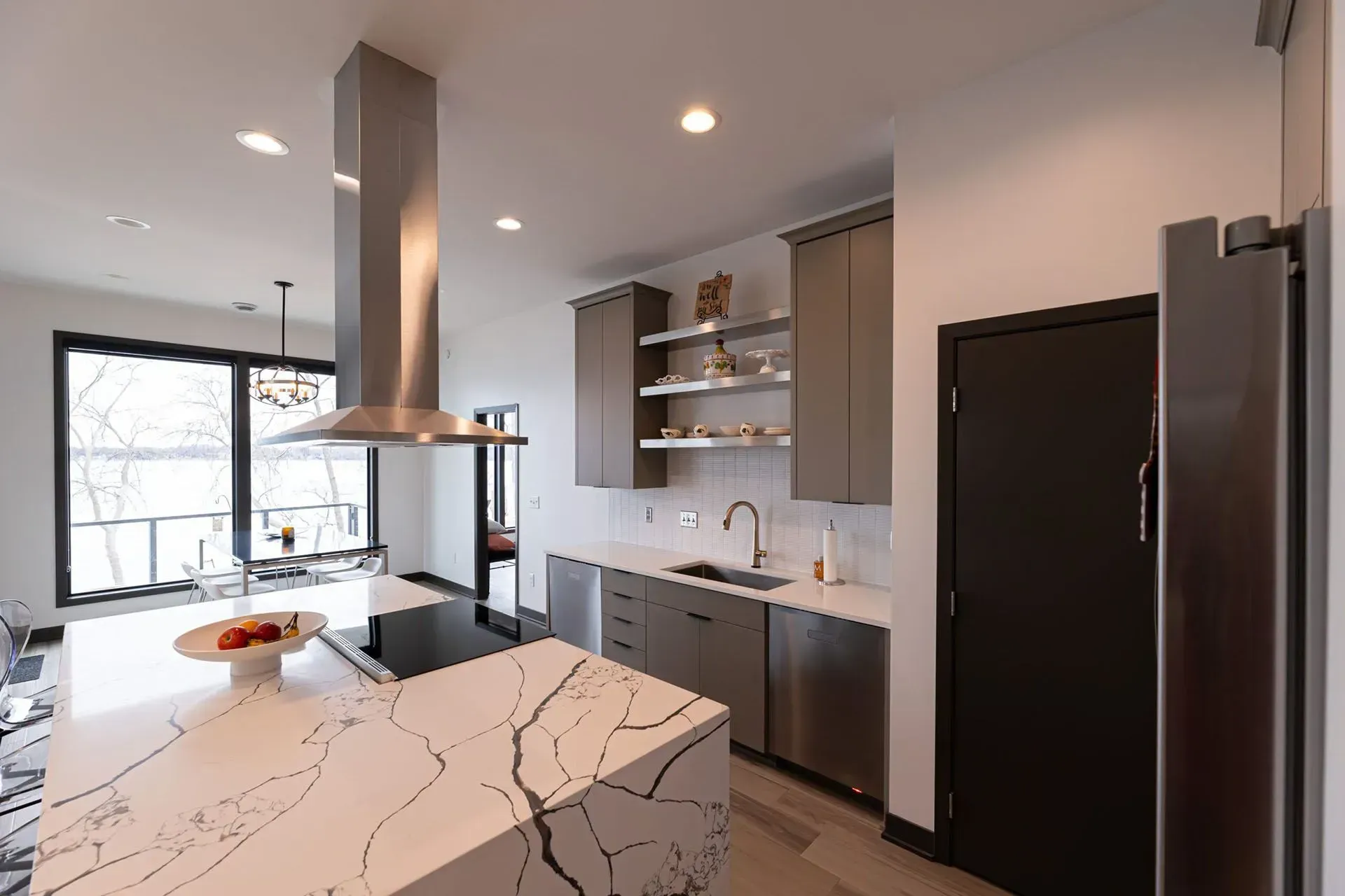 Modern kitchen with island, stainless steel appliances, and large windows.