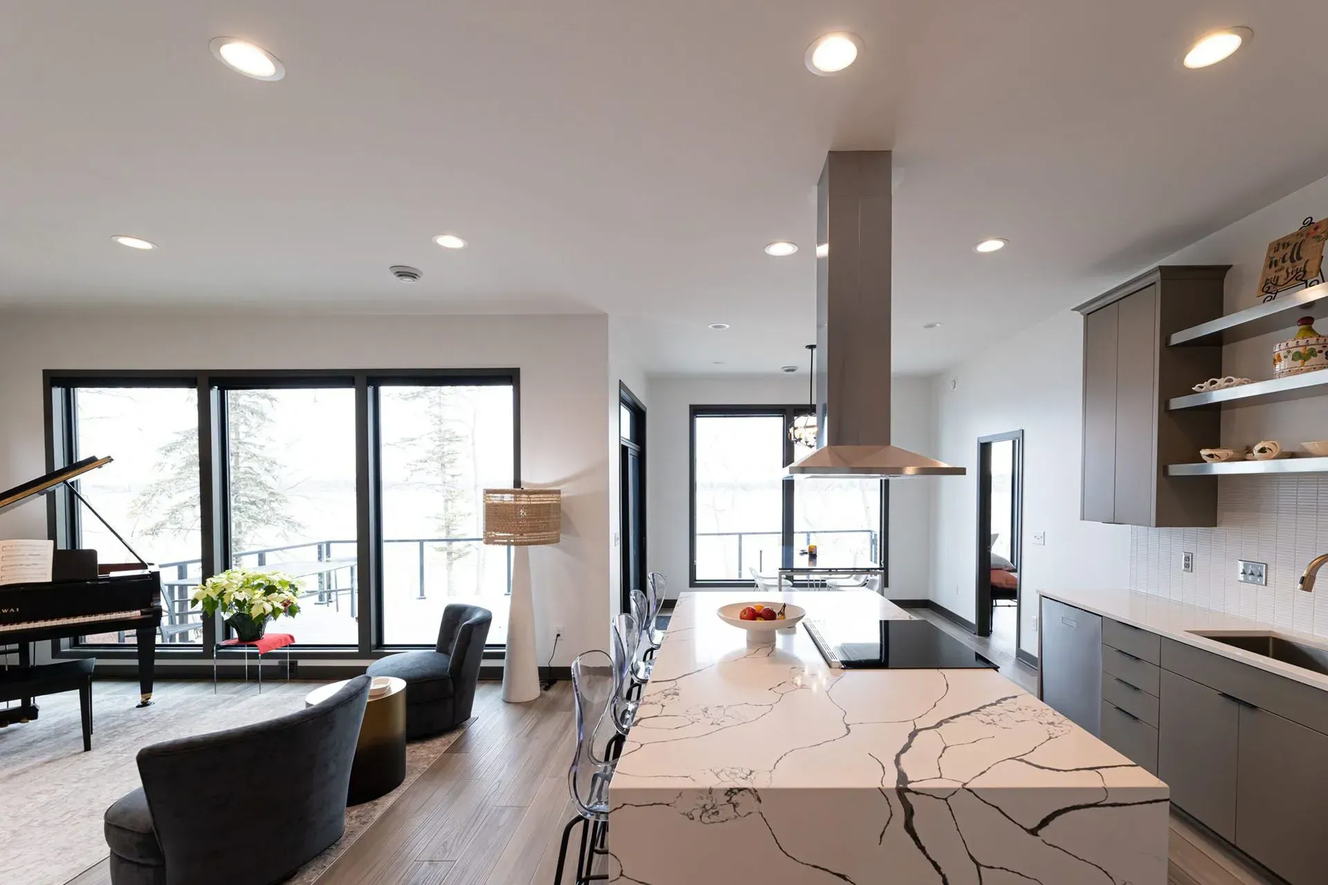 Modern open-plan kitchen with a large island, stainless steel range hood, and piano in the living area.