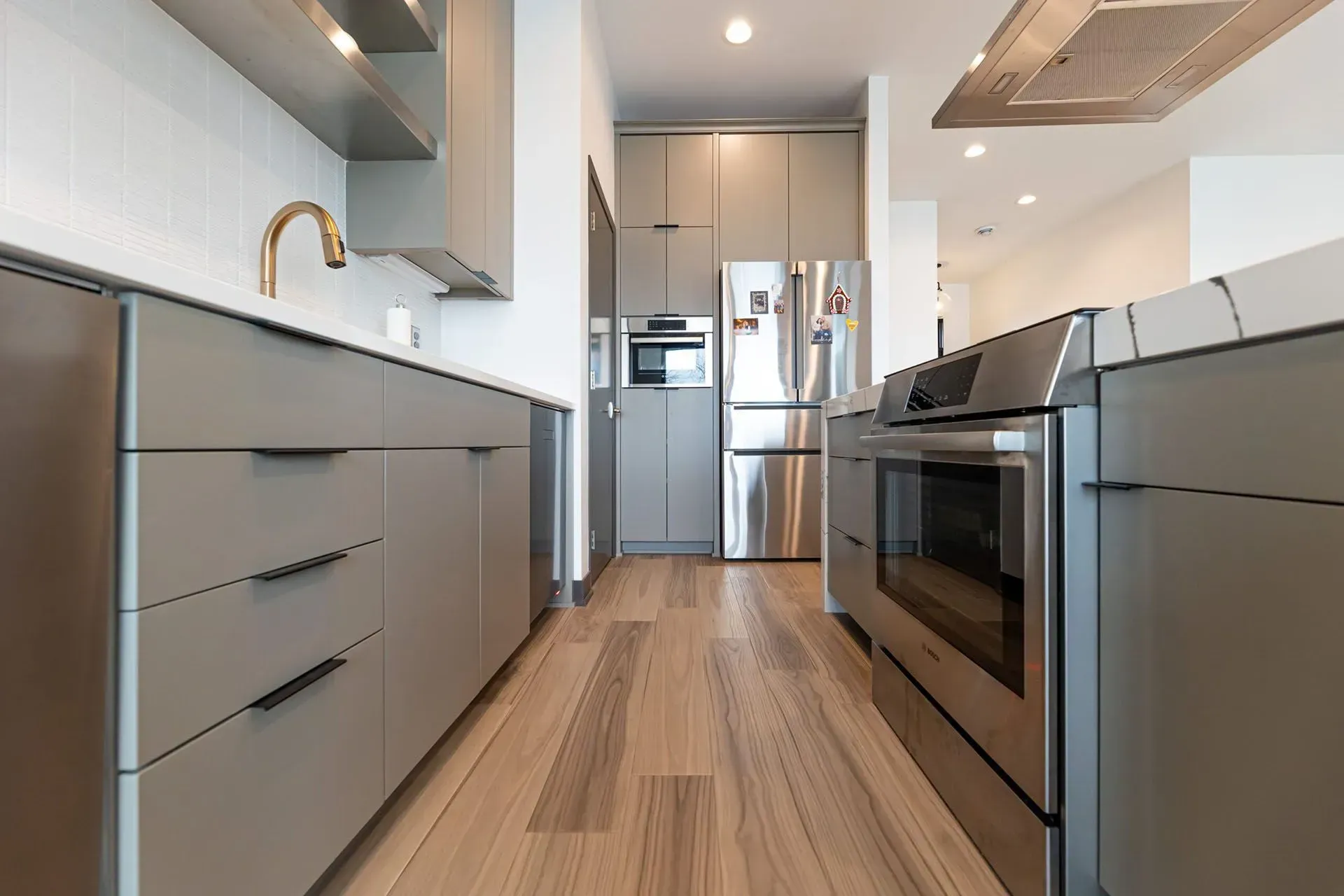 Modern kitchen with gray cabinets, stainless steel appliances, and wood flooring.