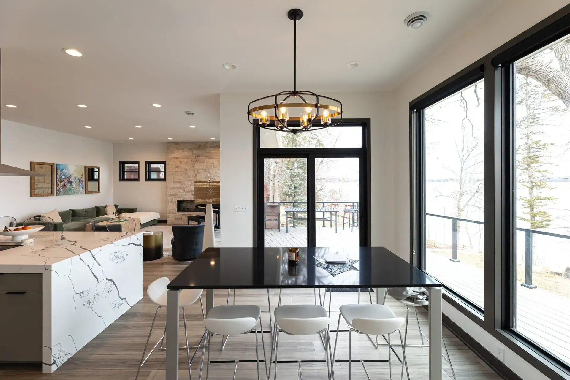 Modern dining area with table, chairs, and large windows overlooking outdoor deck and trees.
