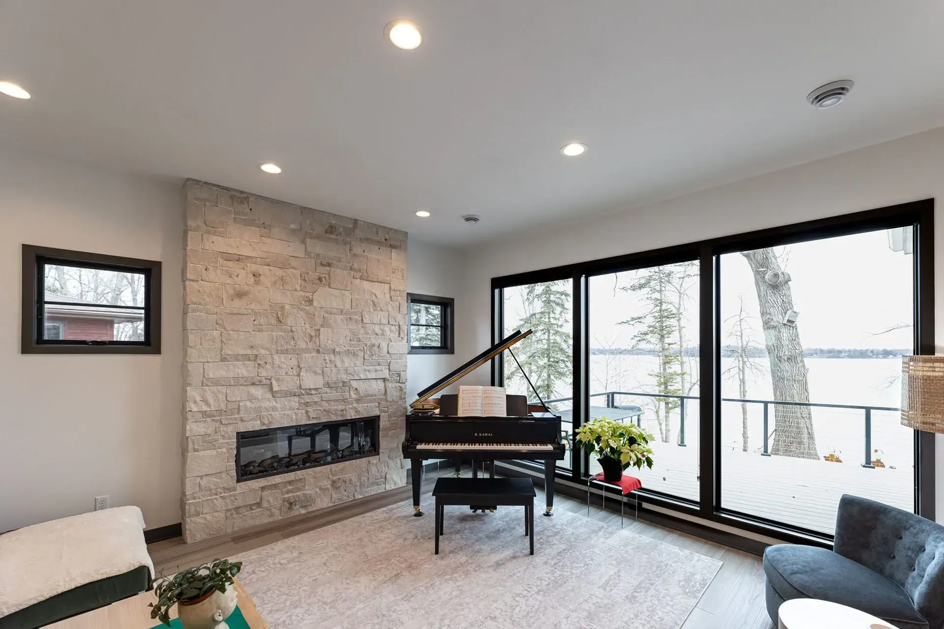 Living room with a grand piano, stone fireplace, and large windows overlooking a lake.