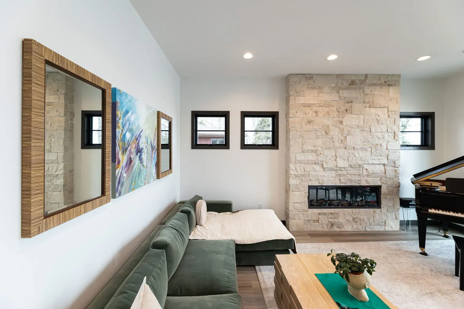 Living room with green sofa, stone fireplace, piano, and art.
