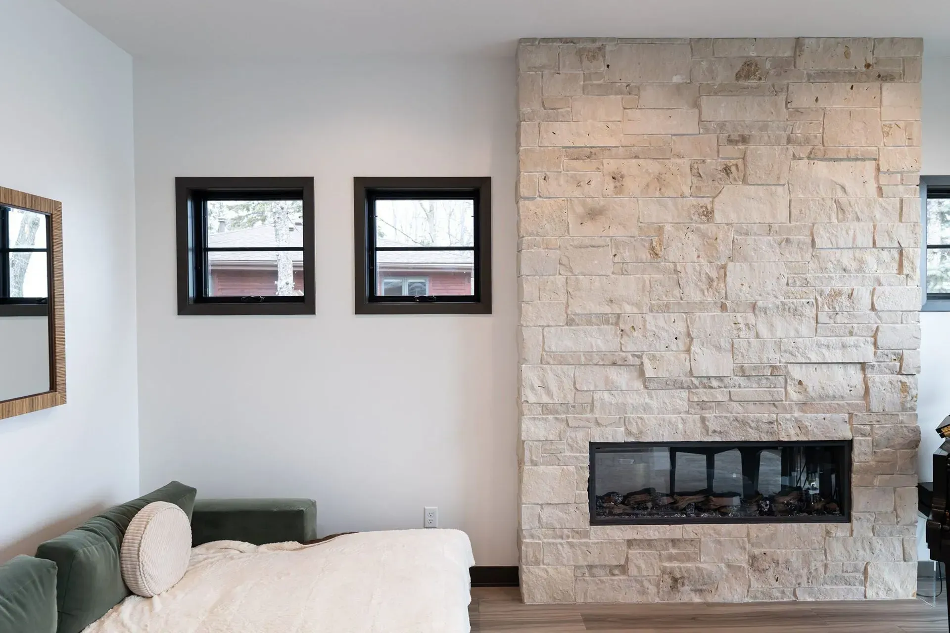 Living room with stone fireplace, two black-framed windows, white wall, green couch, and mirror.