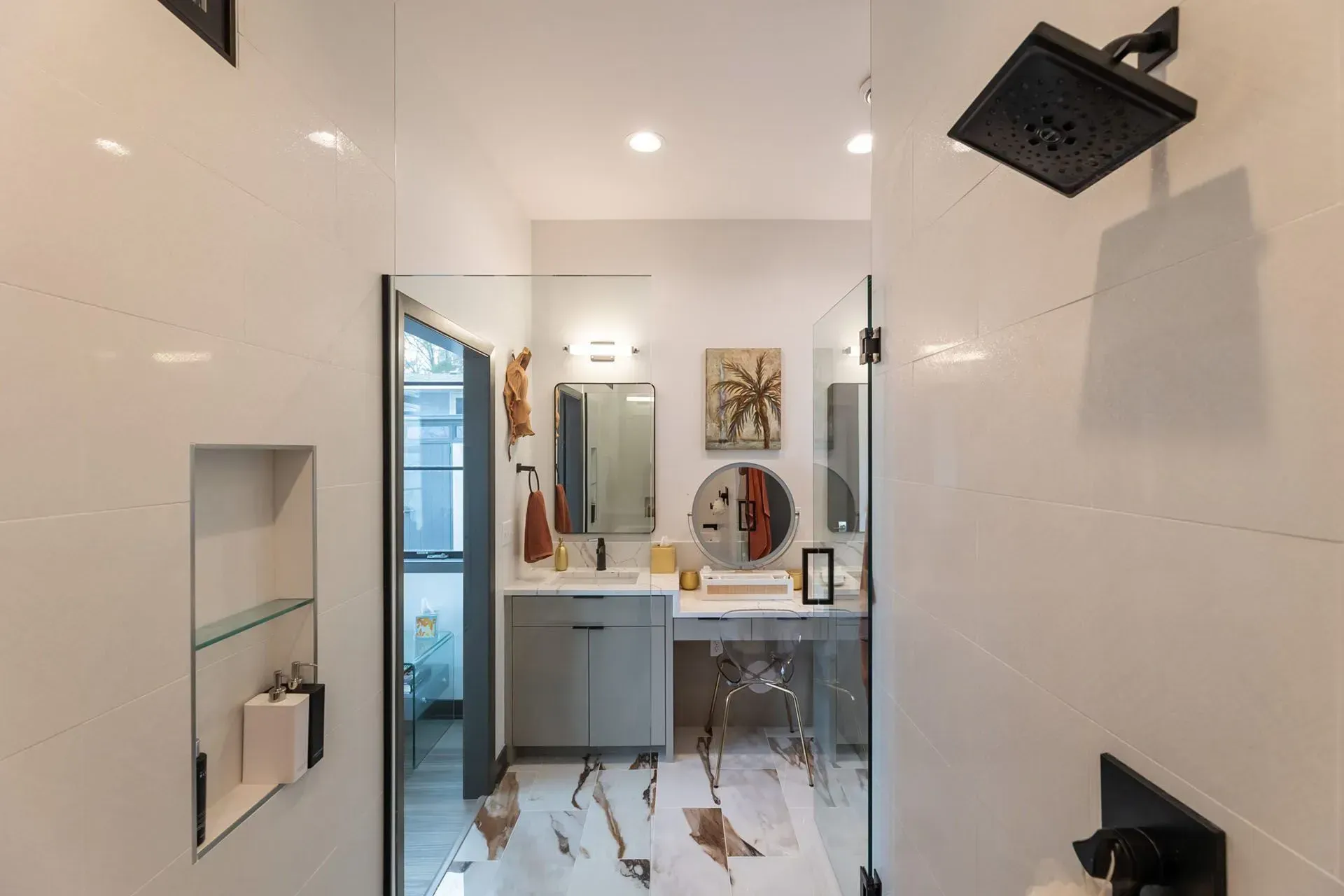 Modern bathroom with white tiled walls, glass shower door, and vanity with mirror.