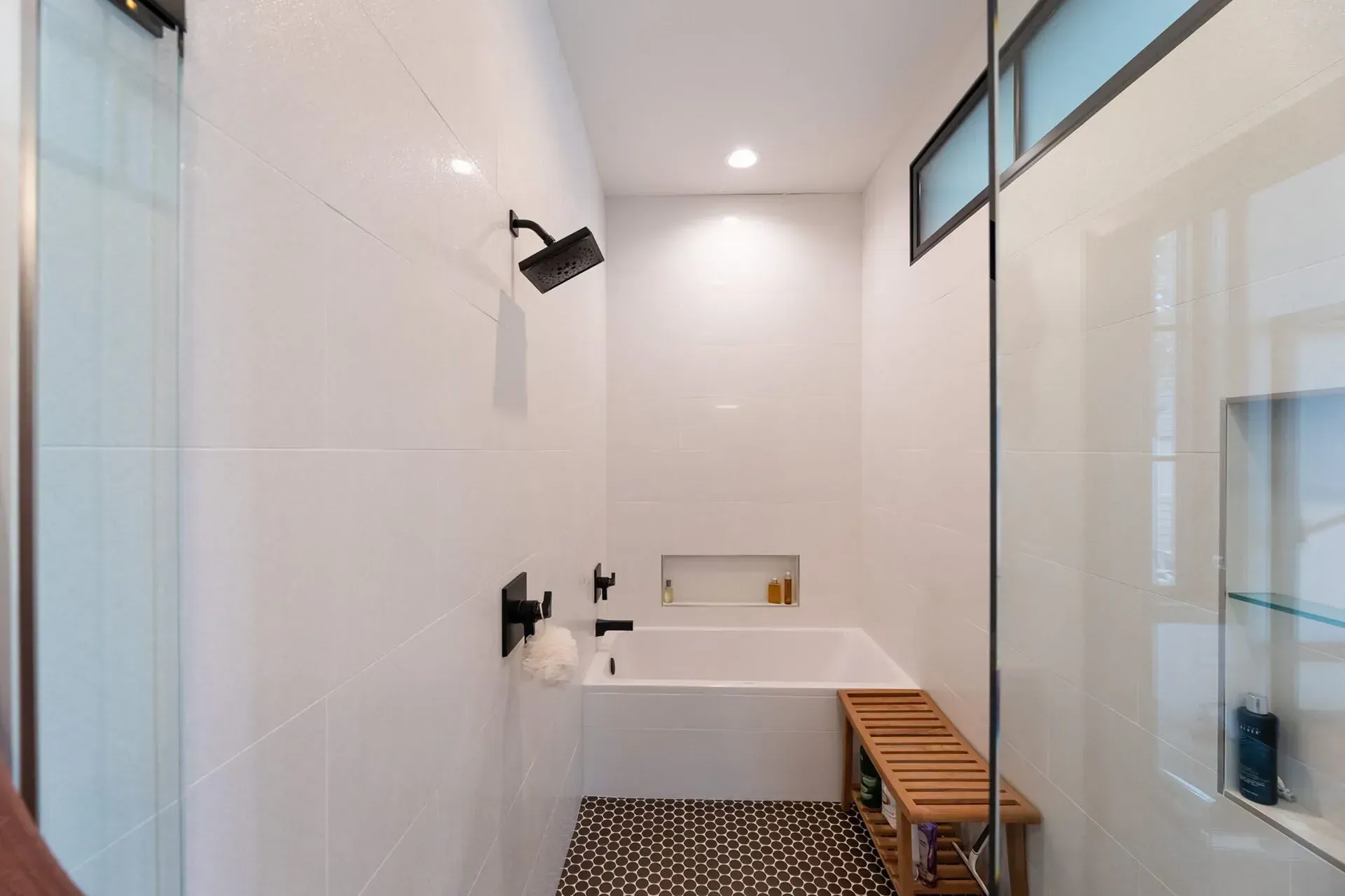 Modern white bathroom with black fixtures, including a showerhead and tub faucet. Small window.