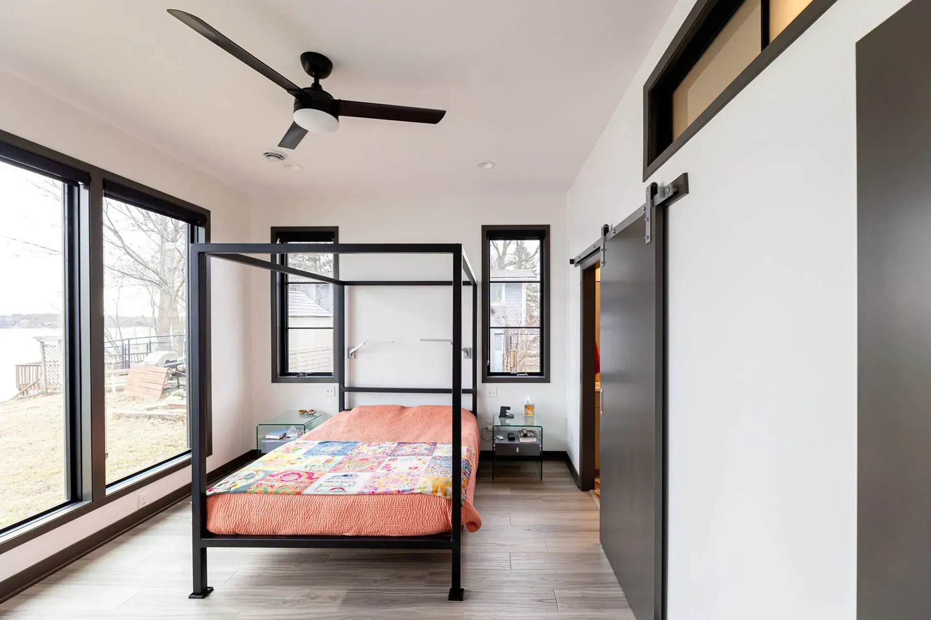 Bedroom with black canopy bed, large windows, sliding door, and gray wood-look flooring.