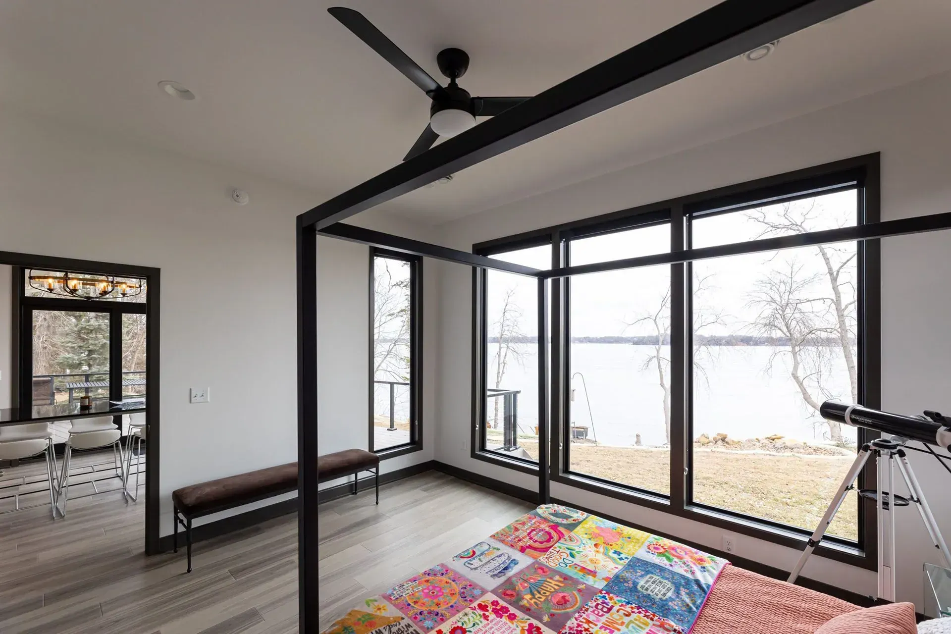 Bedroom with large windows overlooking a lake, four-poster bed, bench, and a telescope.