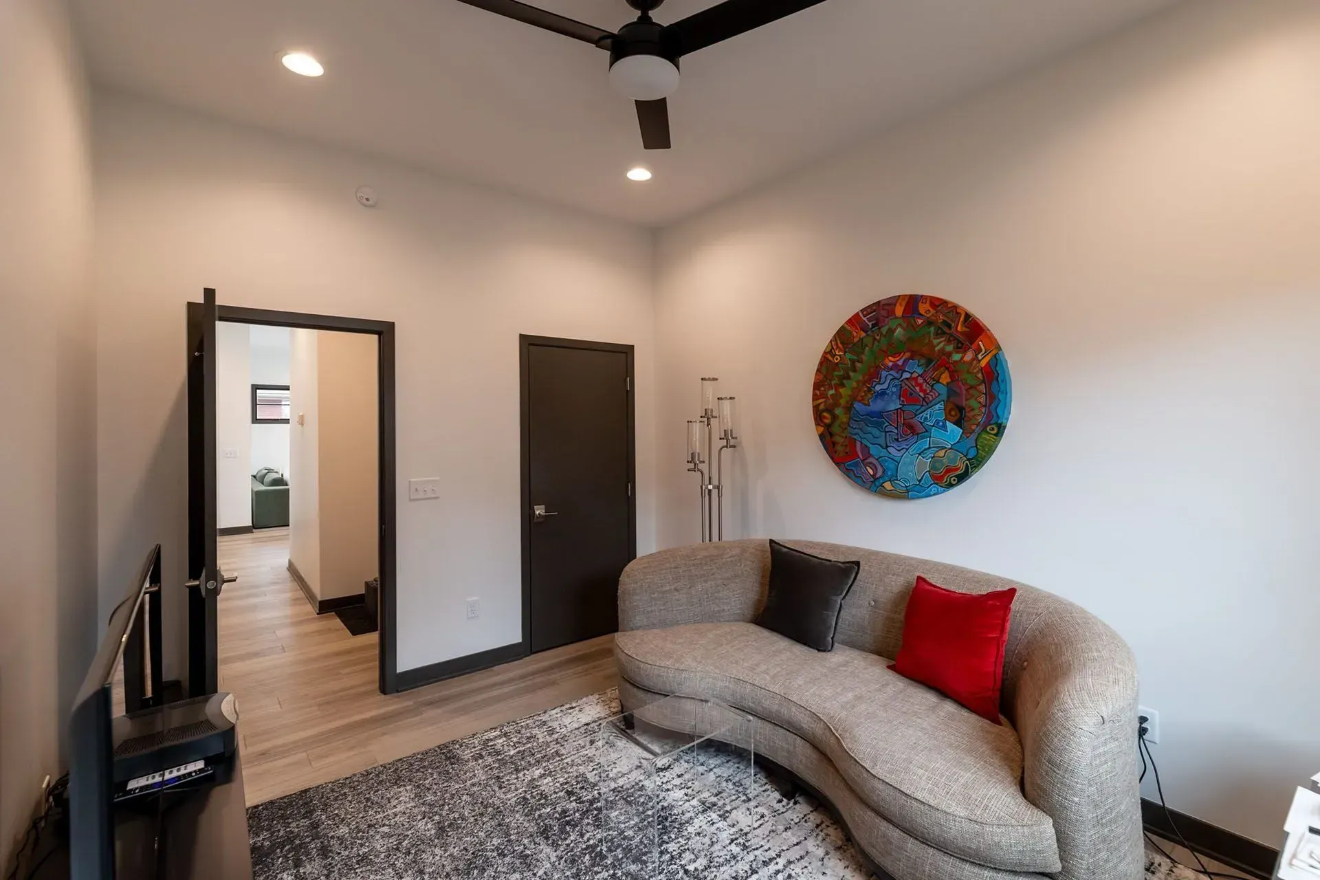 A living room with a curved sofa, rug, colorful art, and an open doorway.