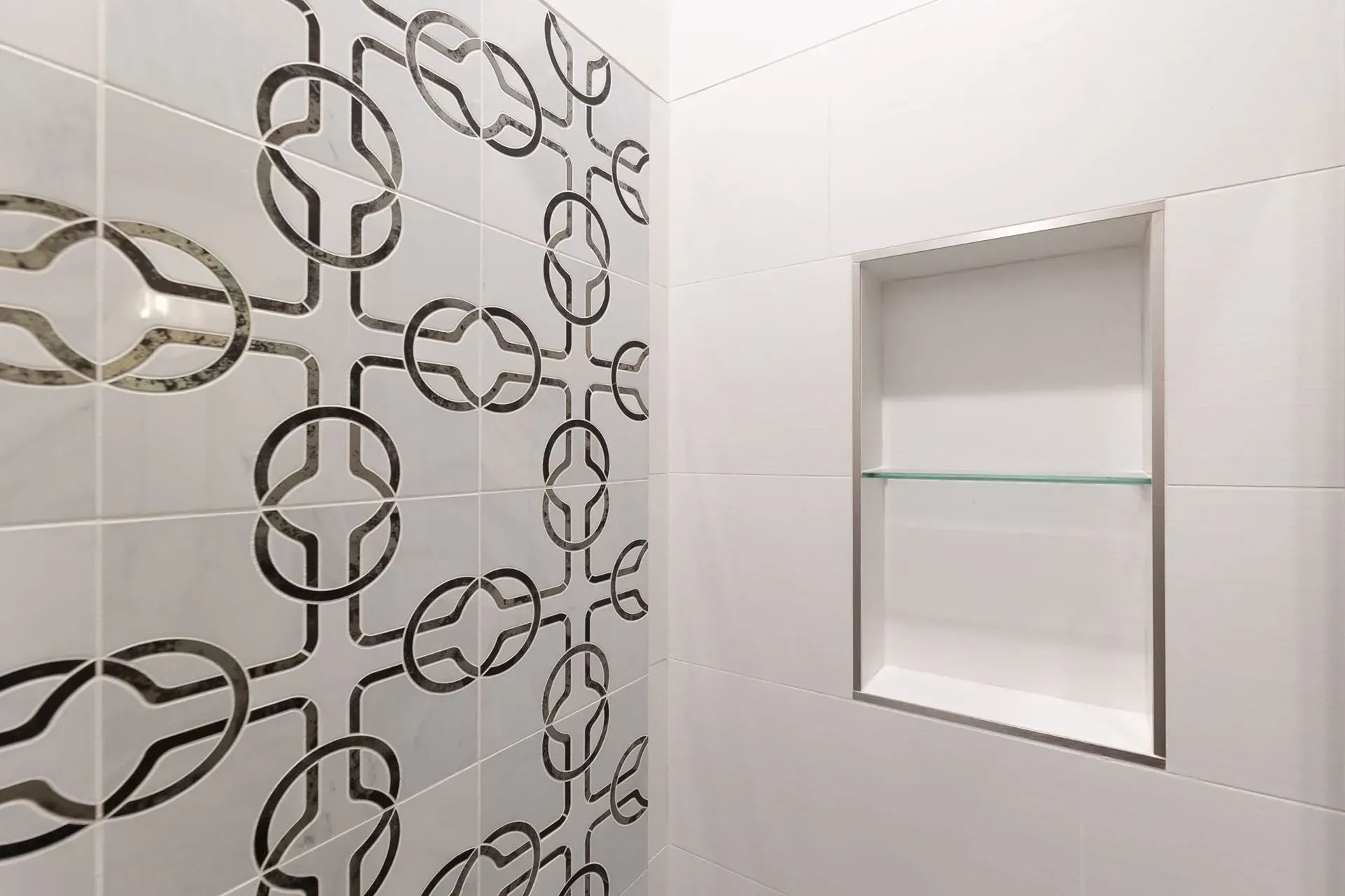 White tile shower with decorative accent tiles and built-in shelf.
