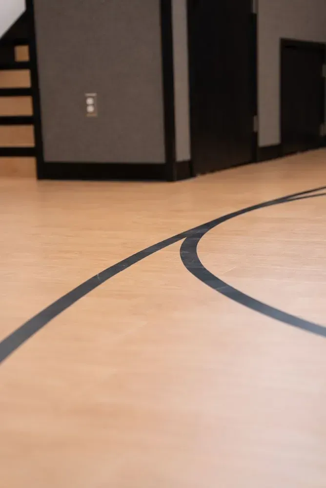 Light wood floor with black lines forming a curve, near a gray wall and stairs.