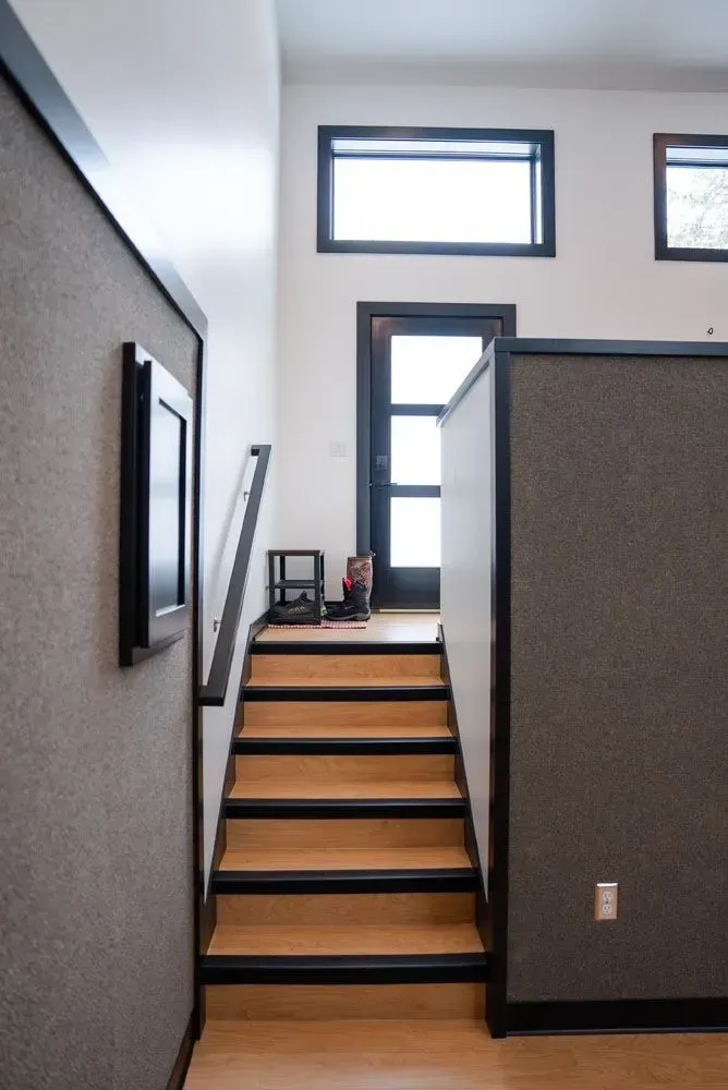 Staircase leading to a door, flanked by gray walls with black trim. Wooden stairs, neutral color palette.