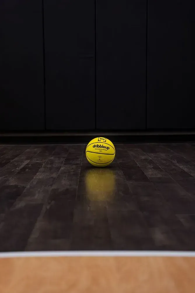 Yellow basketball on a dark wood floor in front of a black wall.