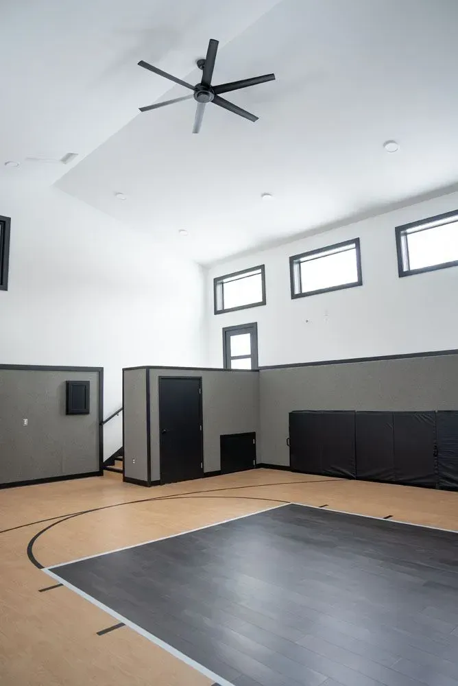 Interior view of a modern gym with a black and tan floor, black accents, and a ceiling fan.