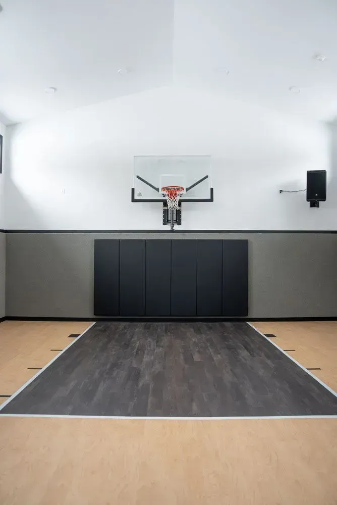 Indoor basketball court with hoop, backboard, padding, and wood flooring.
