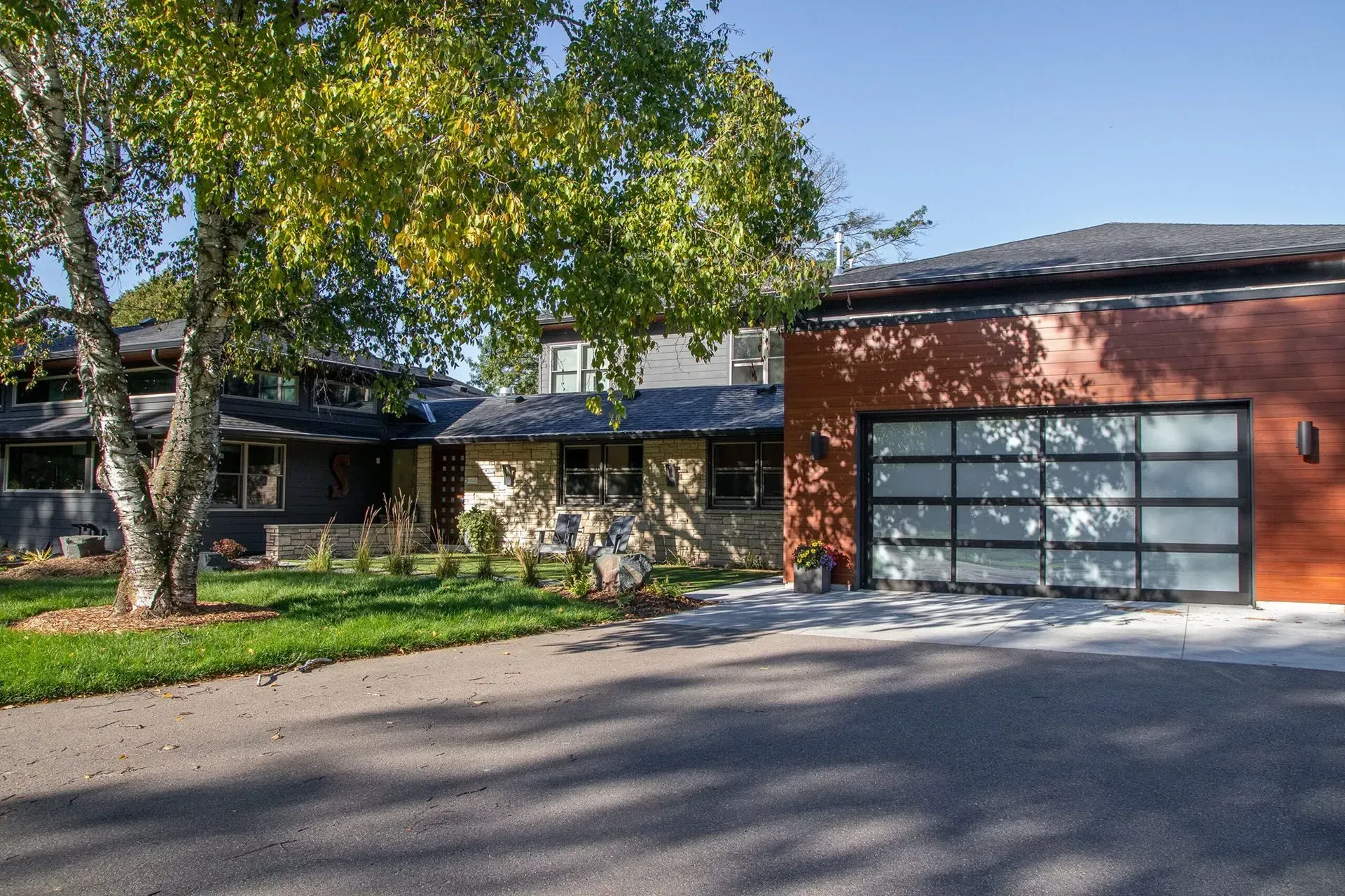 Modern home exterior with a garage and driveway; a tree in the foreground.