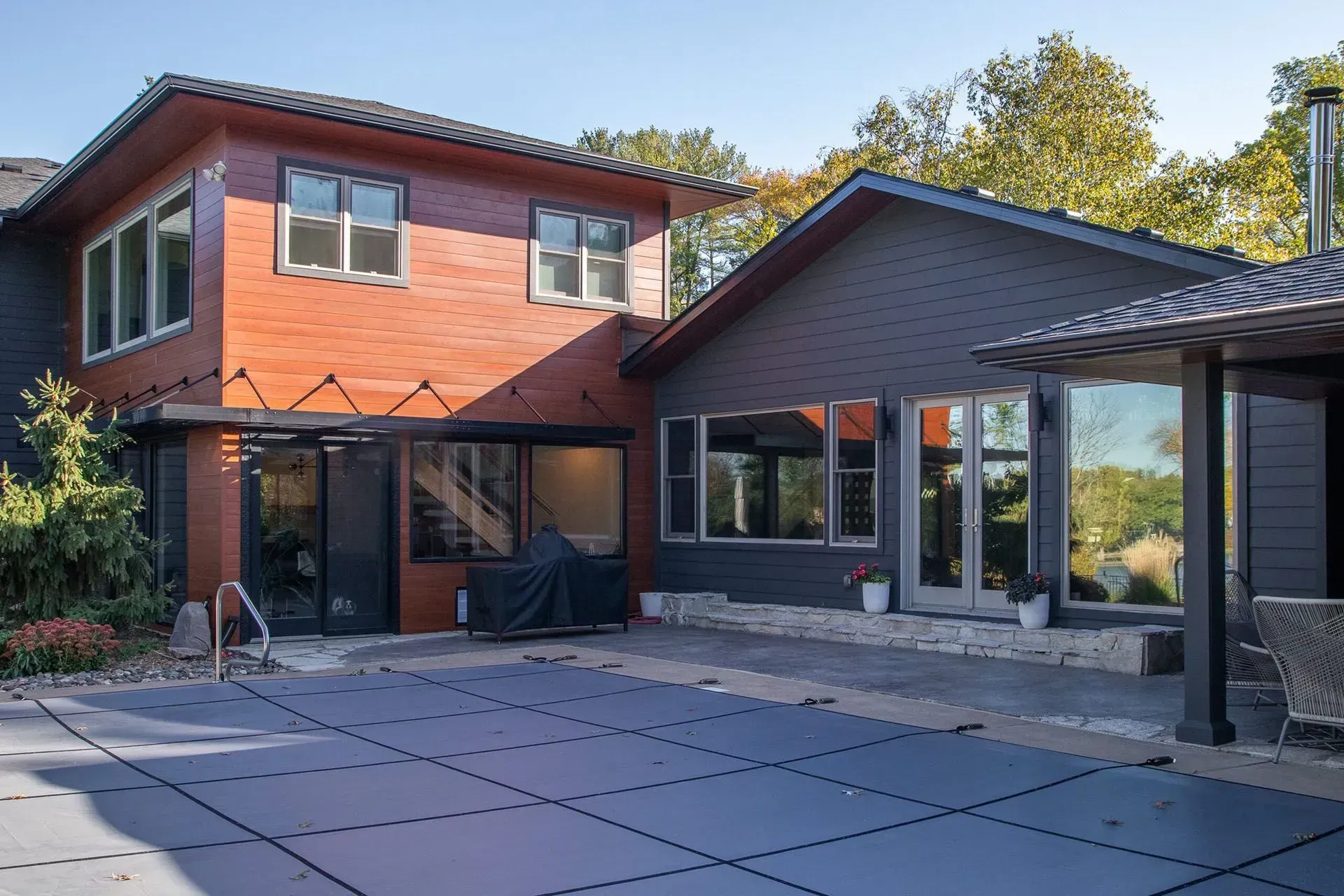 Two-story modern house with a pool and covered patio. The exterior is red and gray, and the pool is covered.