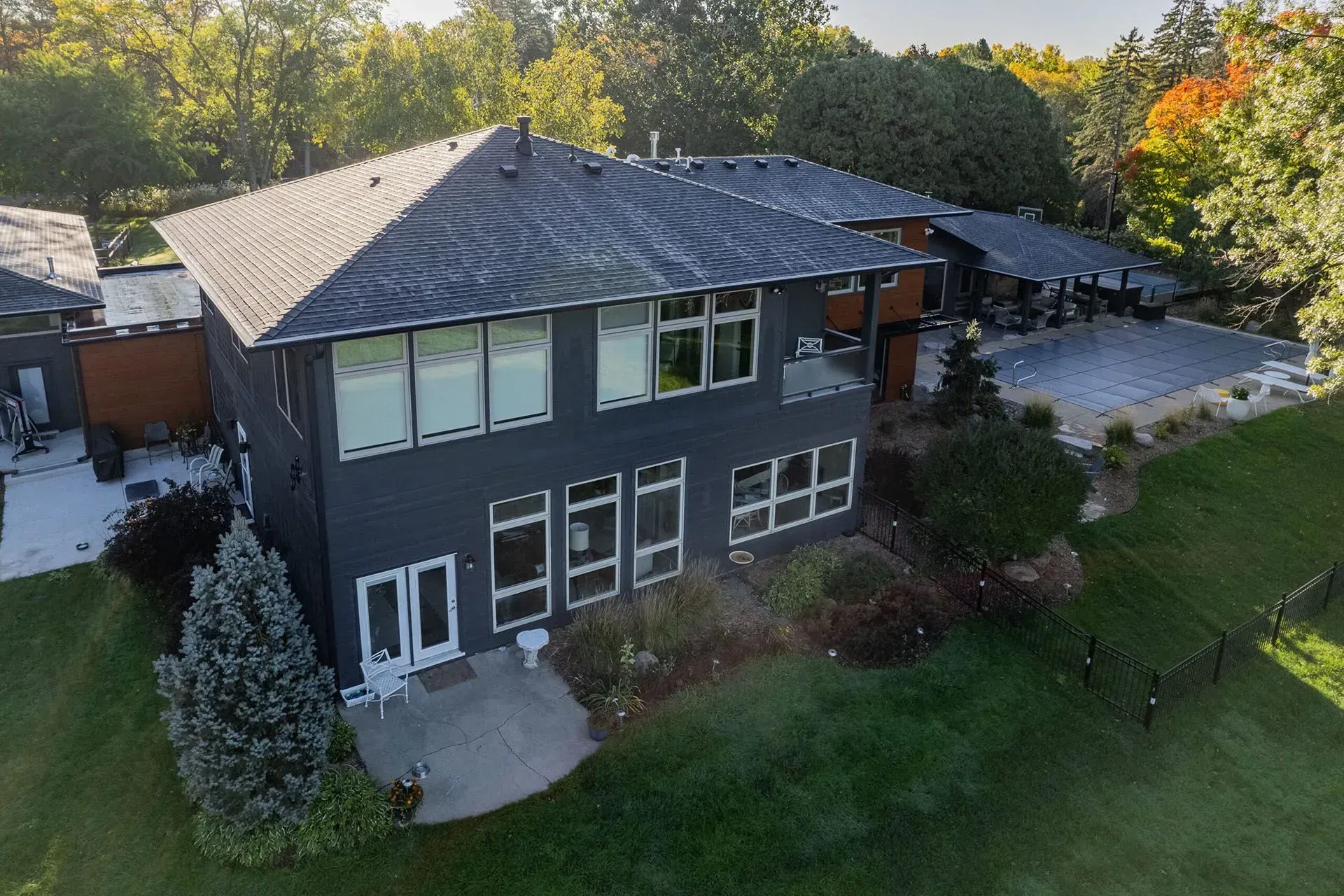 Dark gray two-story house with many windows, green lawn, and trees.