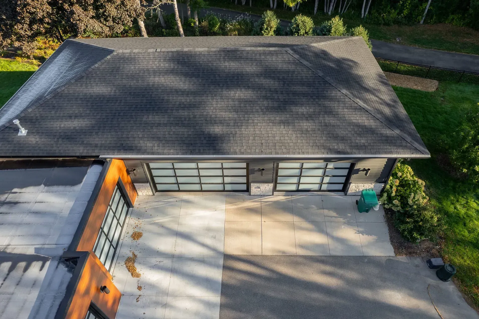 Overhead view of a garage with glass doors and a concrete driveway surrounded by green grass and trees.