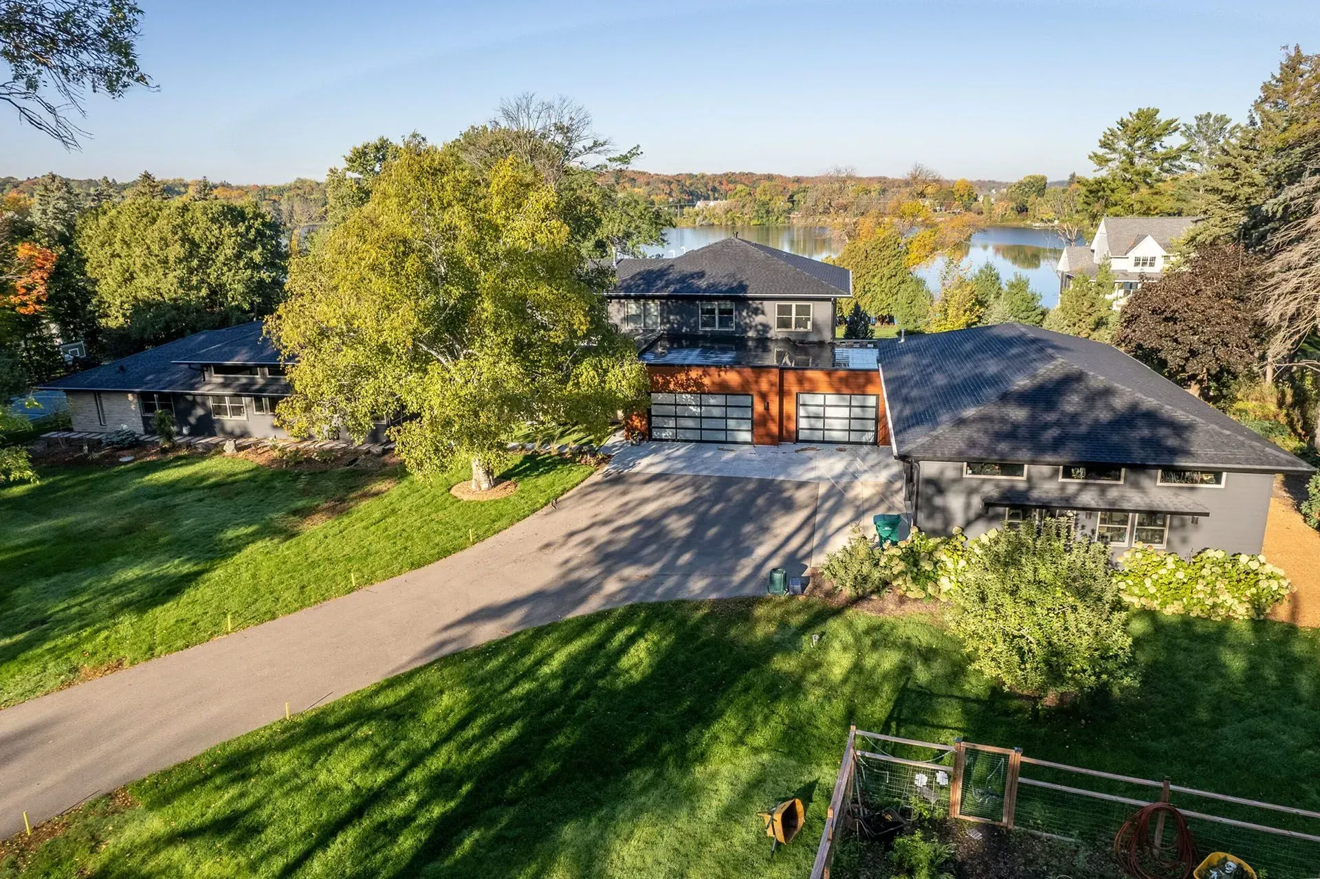 Modern home with black and wood accents, driveway, green lawn, lake view.