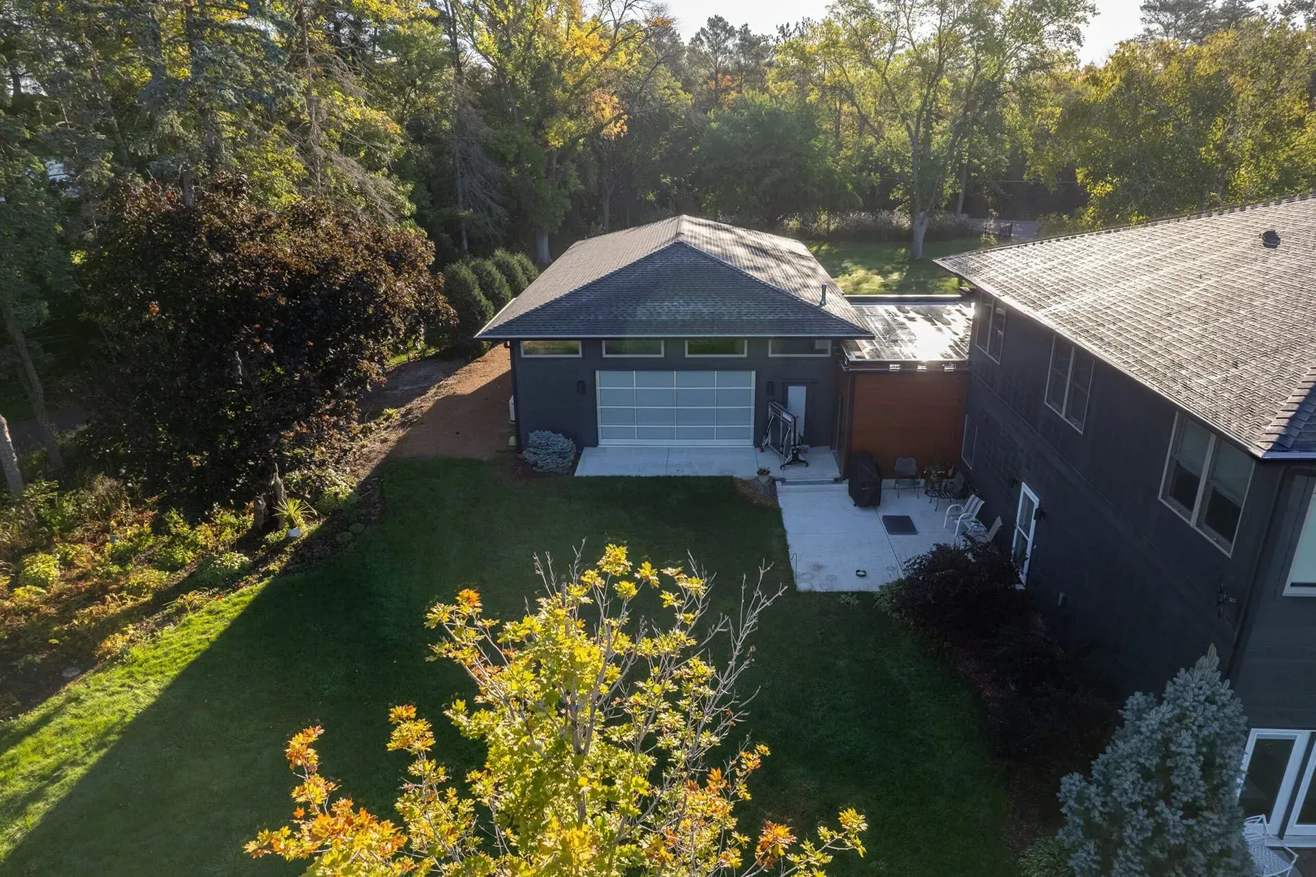 Backyard with modern dark grey detached garage, patio, and lush green lawn.