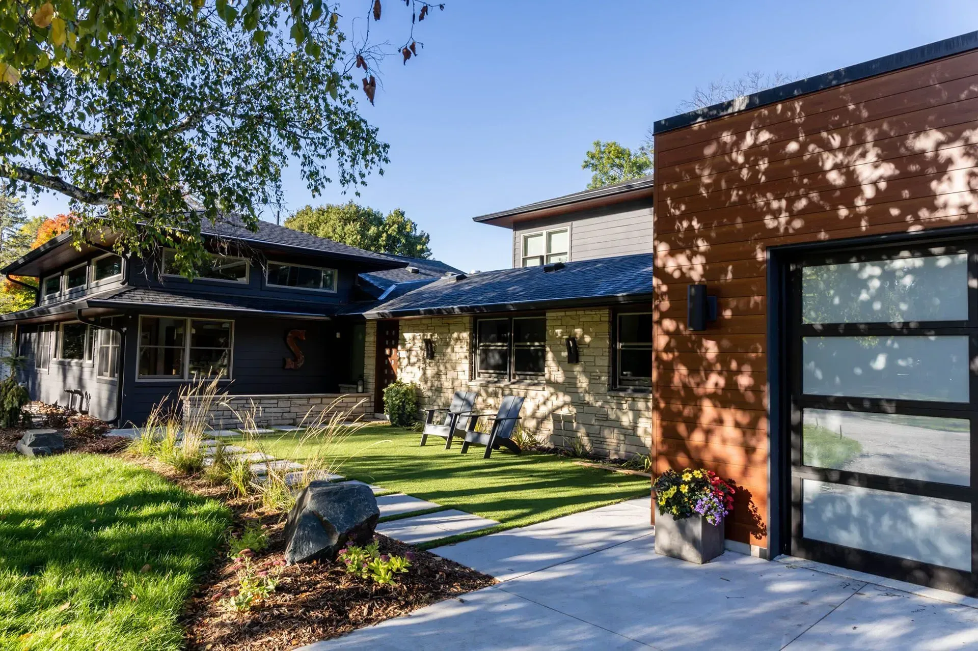 Modern home exterior with a stone and wood facade, blue roof, and a detached garage with a glass door.