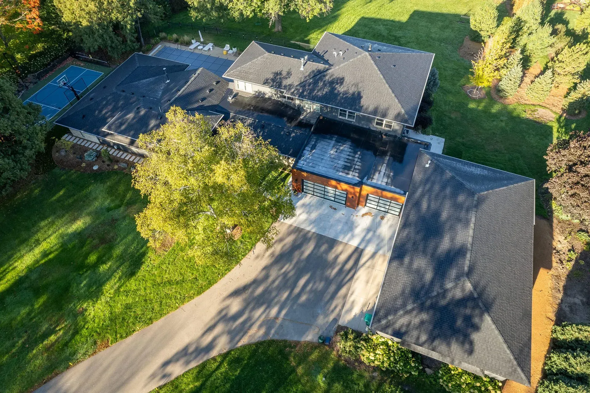 Aerial view of a modern house with a long driveway and dark roof, surrounded by green grass and trees.