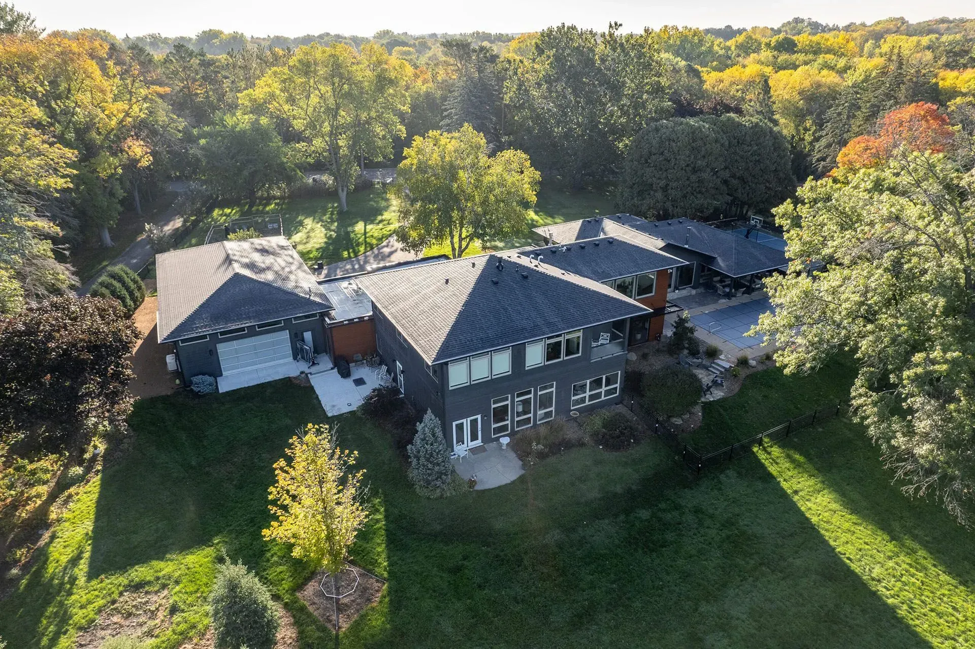 Modern gray house nestled in a green and yellow tree-filled yard on a sunny day.