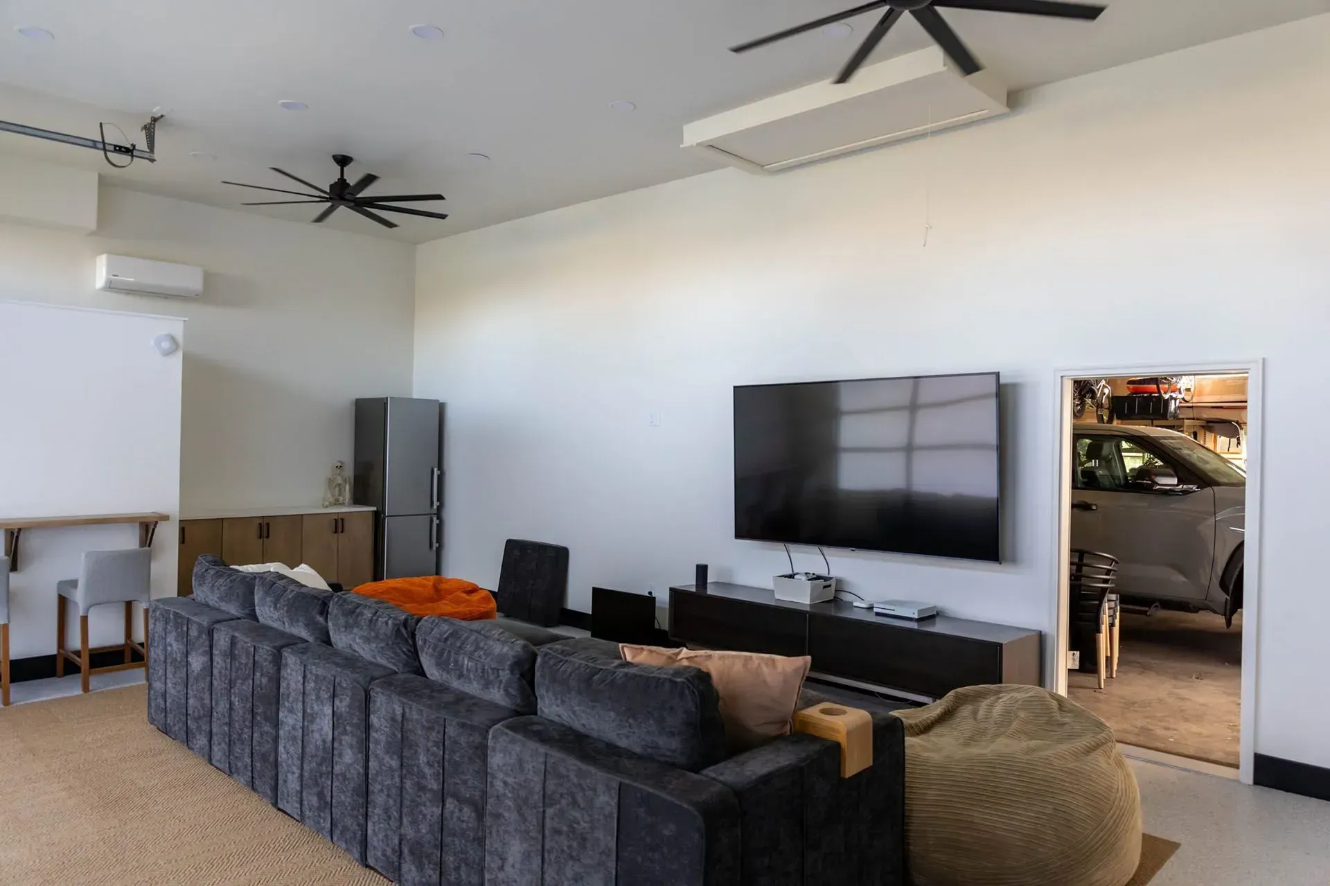 A modern living room with a large sofa, TV, and open garage door revealing a car.