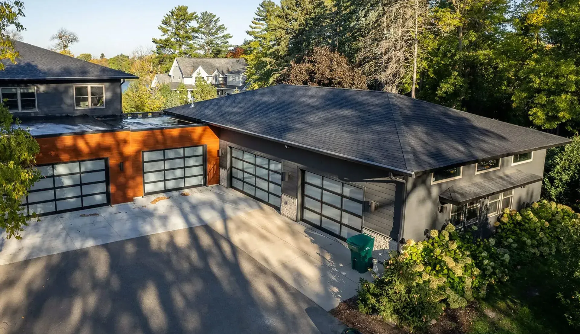 Modern gray house with glass garage doors, orange accent, and black roof.