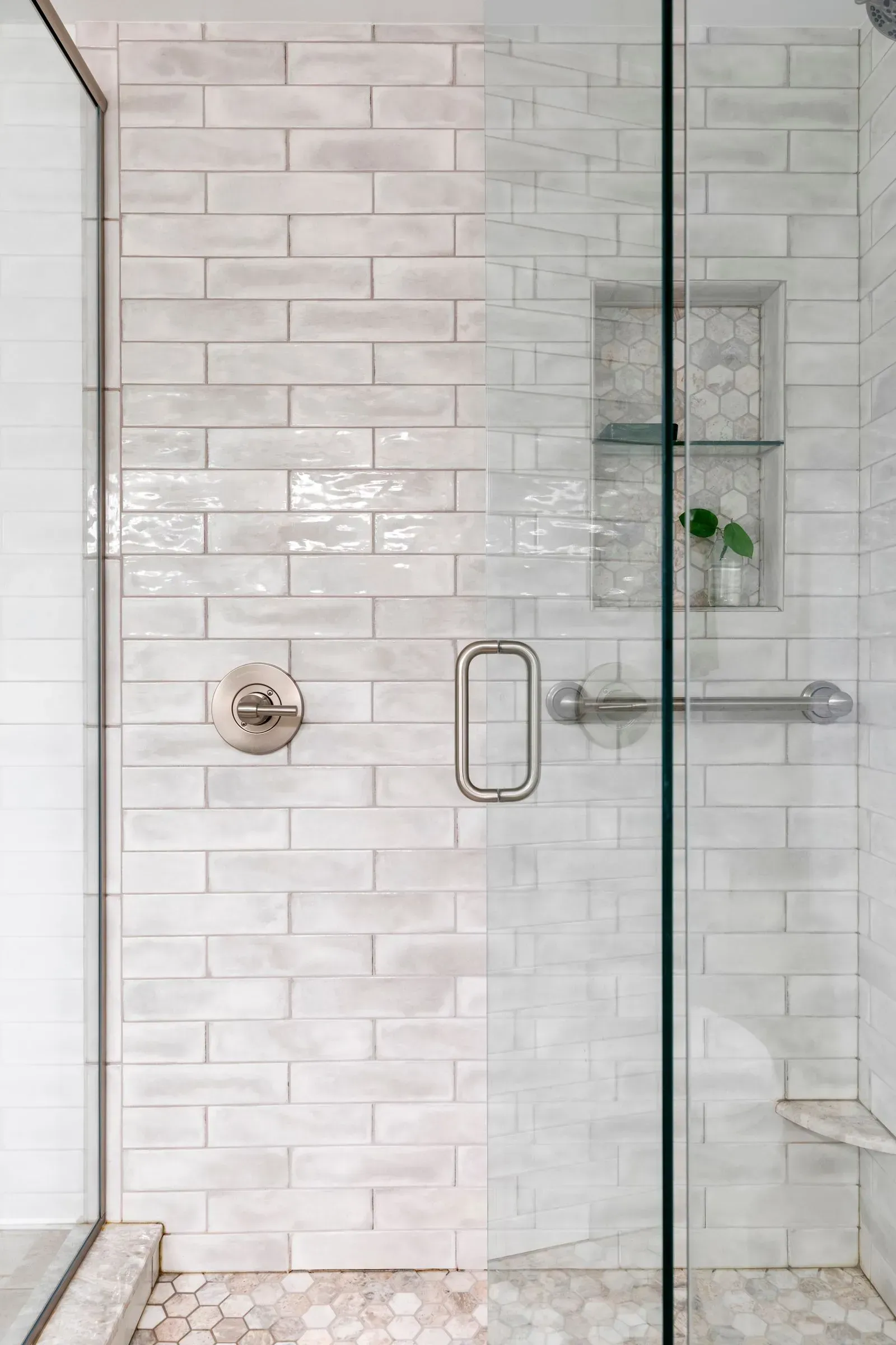 Shower with white brick-like tiles, a glass door, and a built-in shelf.
