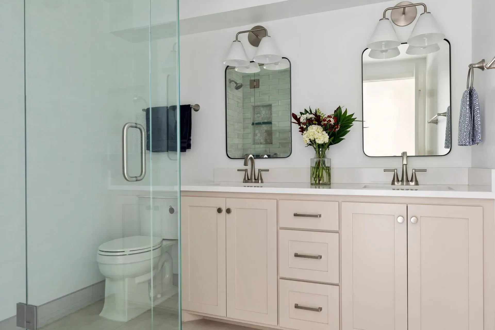 A bright bathroom with a shower, vanity, and toilet. White and cream tones, with silver fixtures.