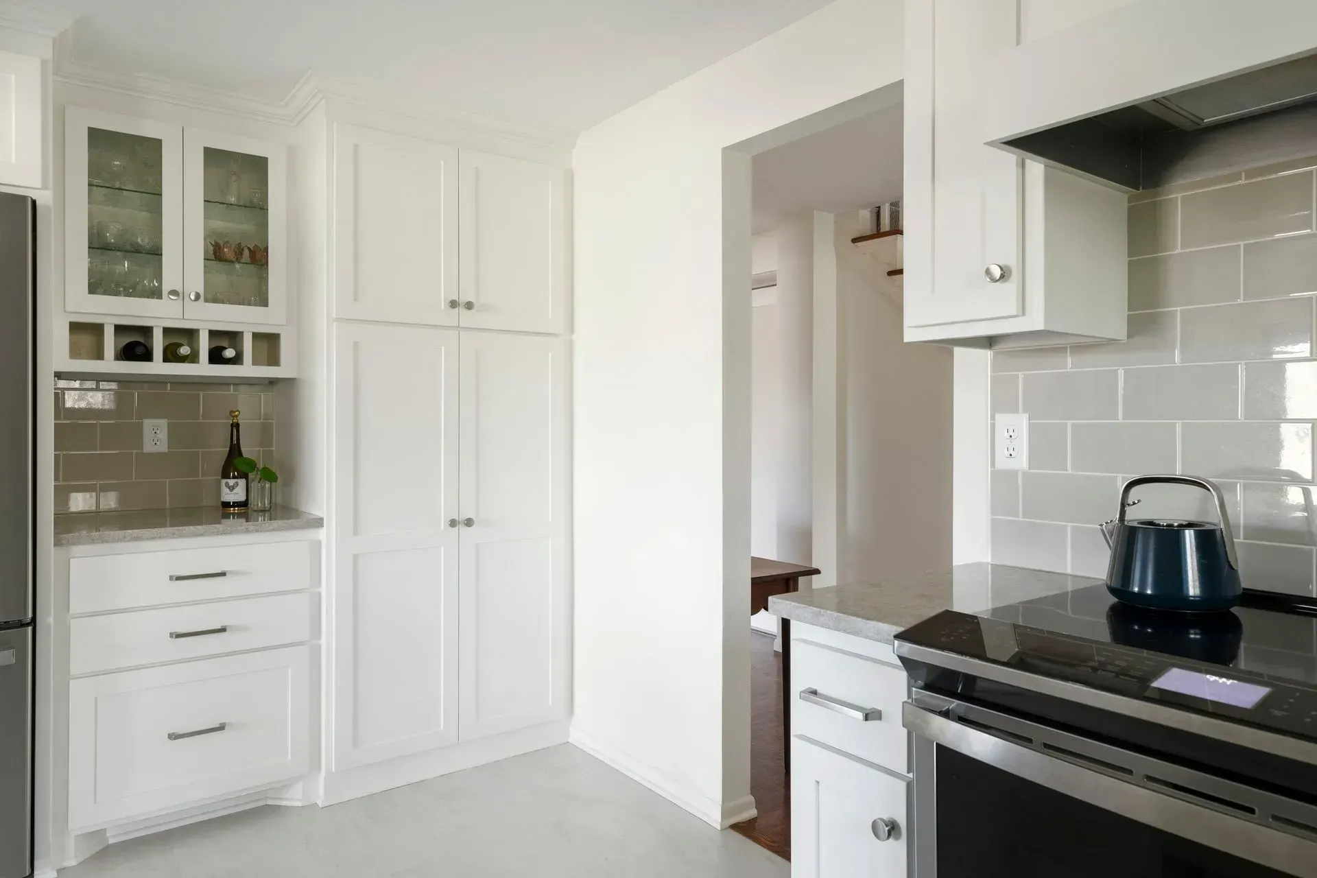 White kitchen with gray tile backsplash, stove, and cabinets.
