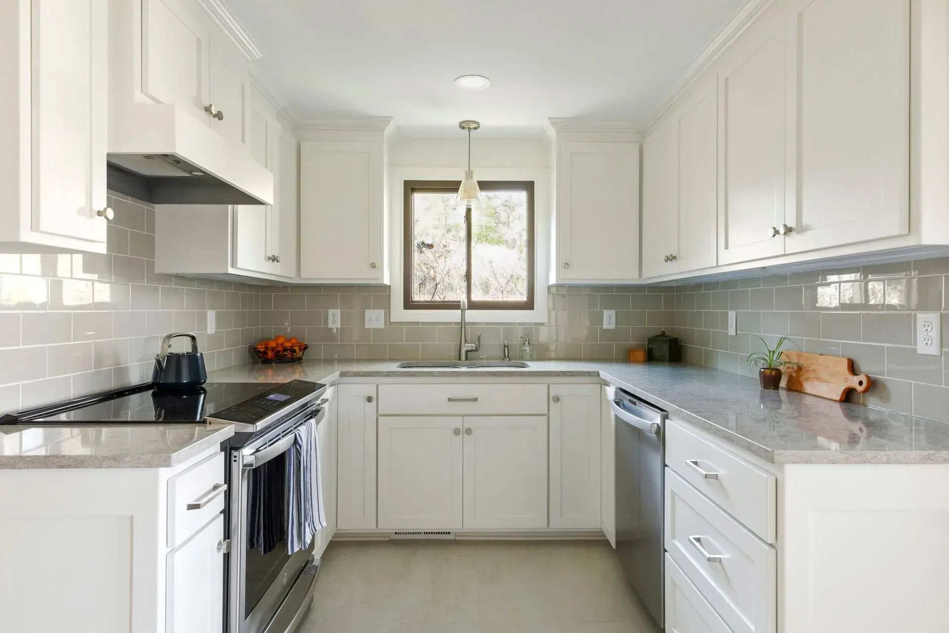 U-shaped kitchen with white cabinets, gray countertops and backsplash, stainless steel appliances, and a window.
