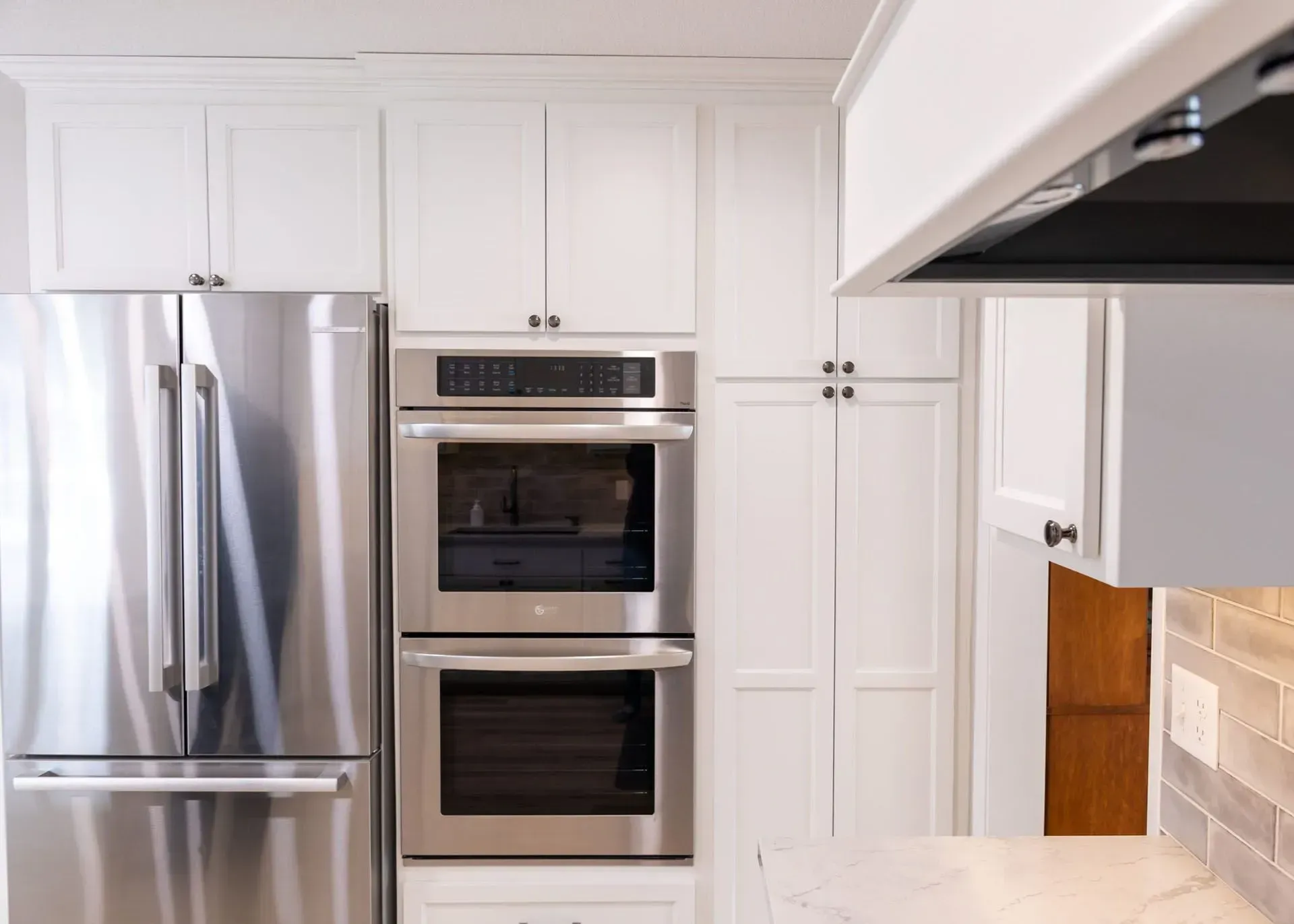 Stainless steel refrigerator, built-in double ovens, and white kitchen cabinets.