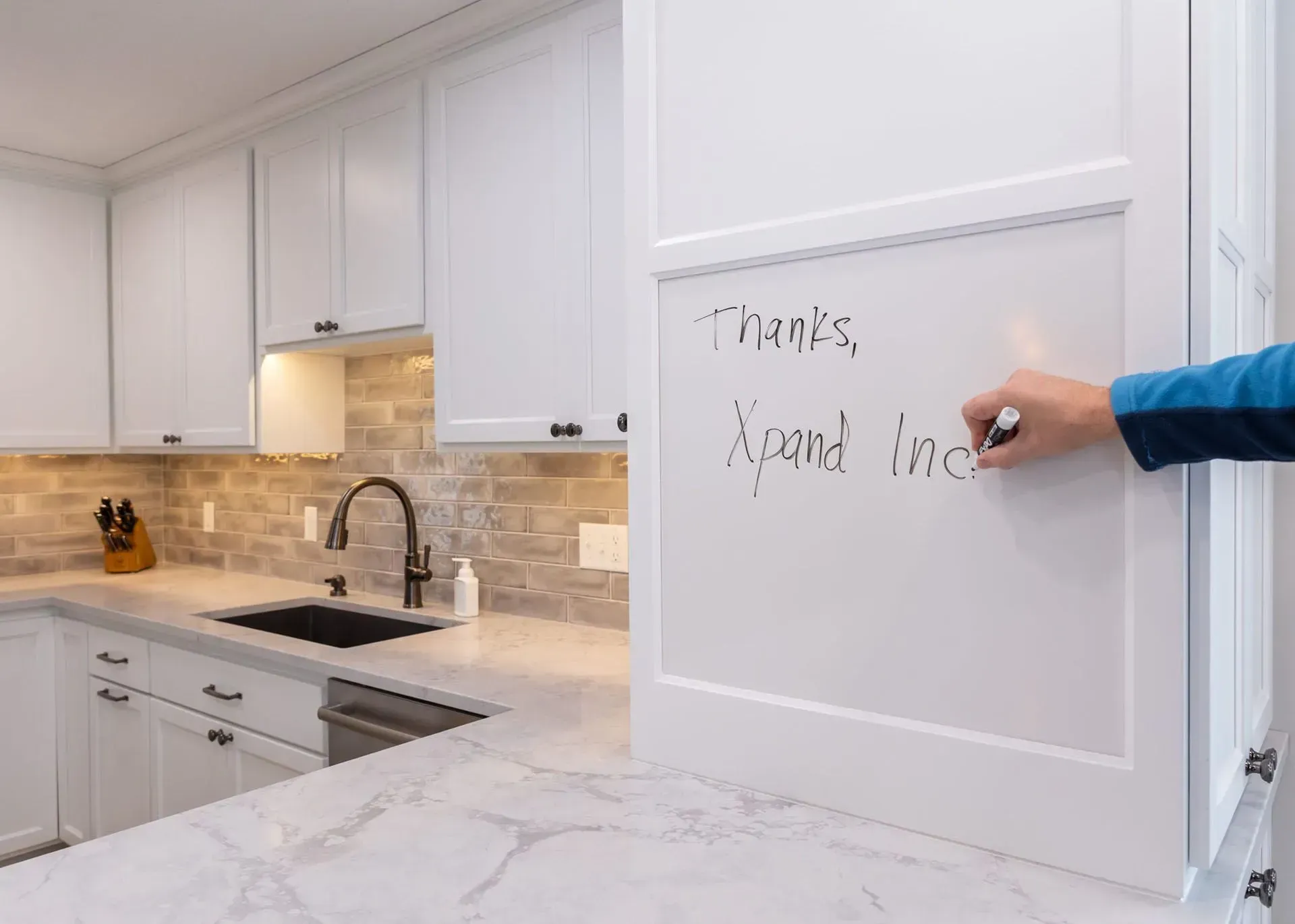 Kitchen with white cabinets and countertop. A hand writes on a white board that is part of a cabinet.
