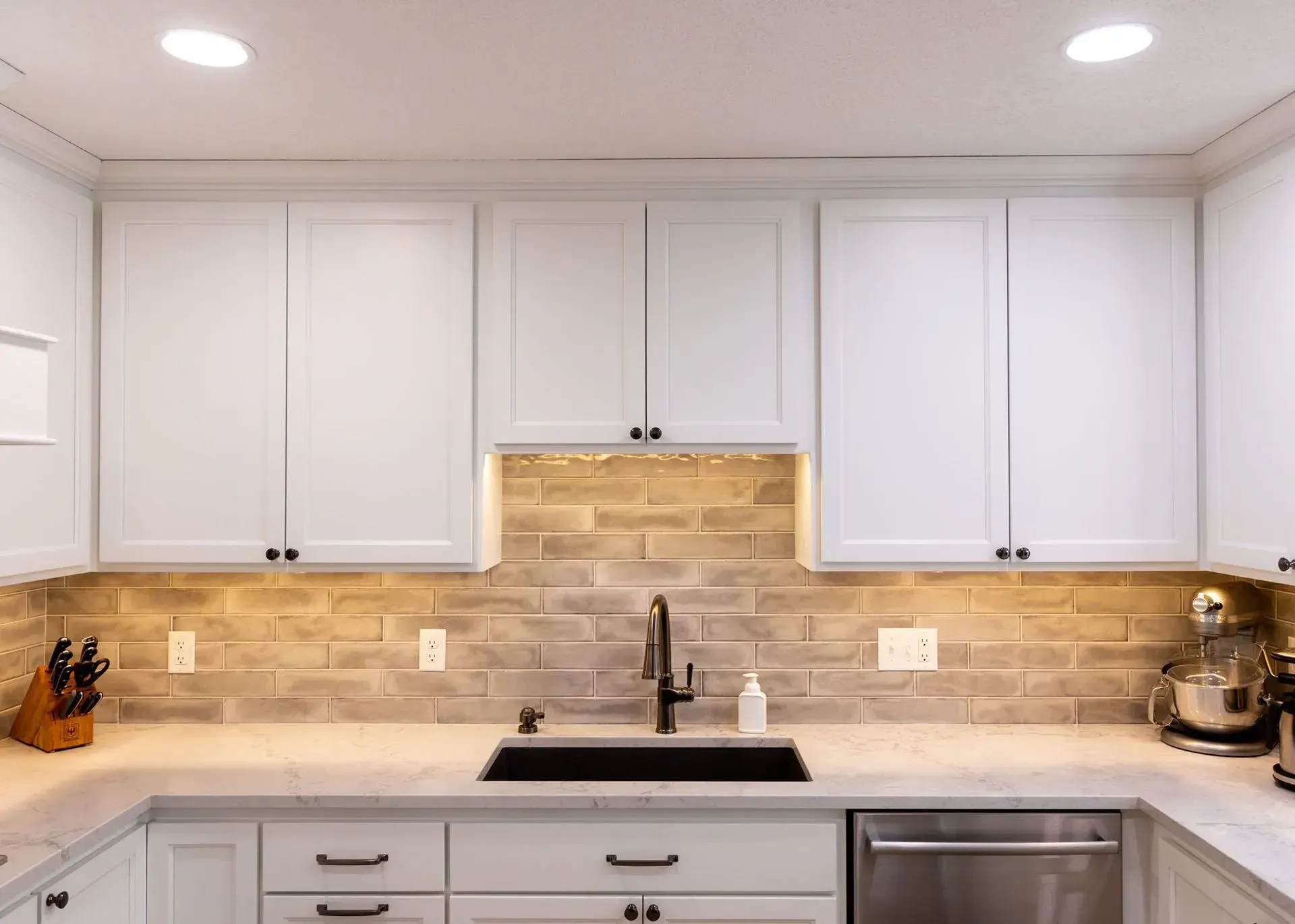 White kitchen cabinets above a brick backsplash with a black faucet and sink.